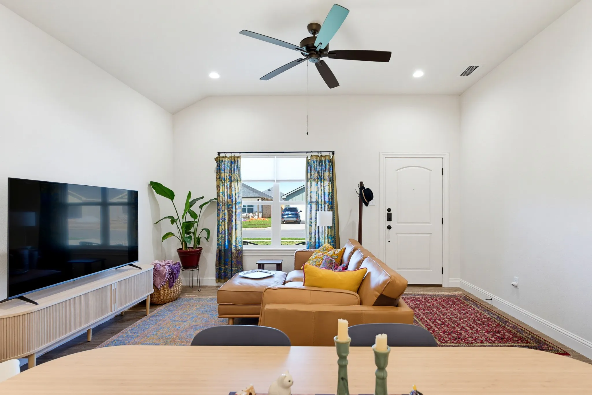 Vaulted ceiling, recessed lighting, ceiling fan, front entry door, and large window