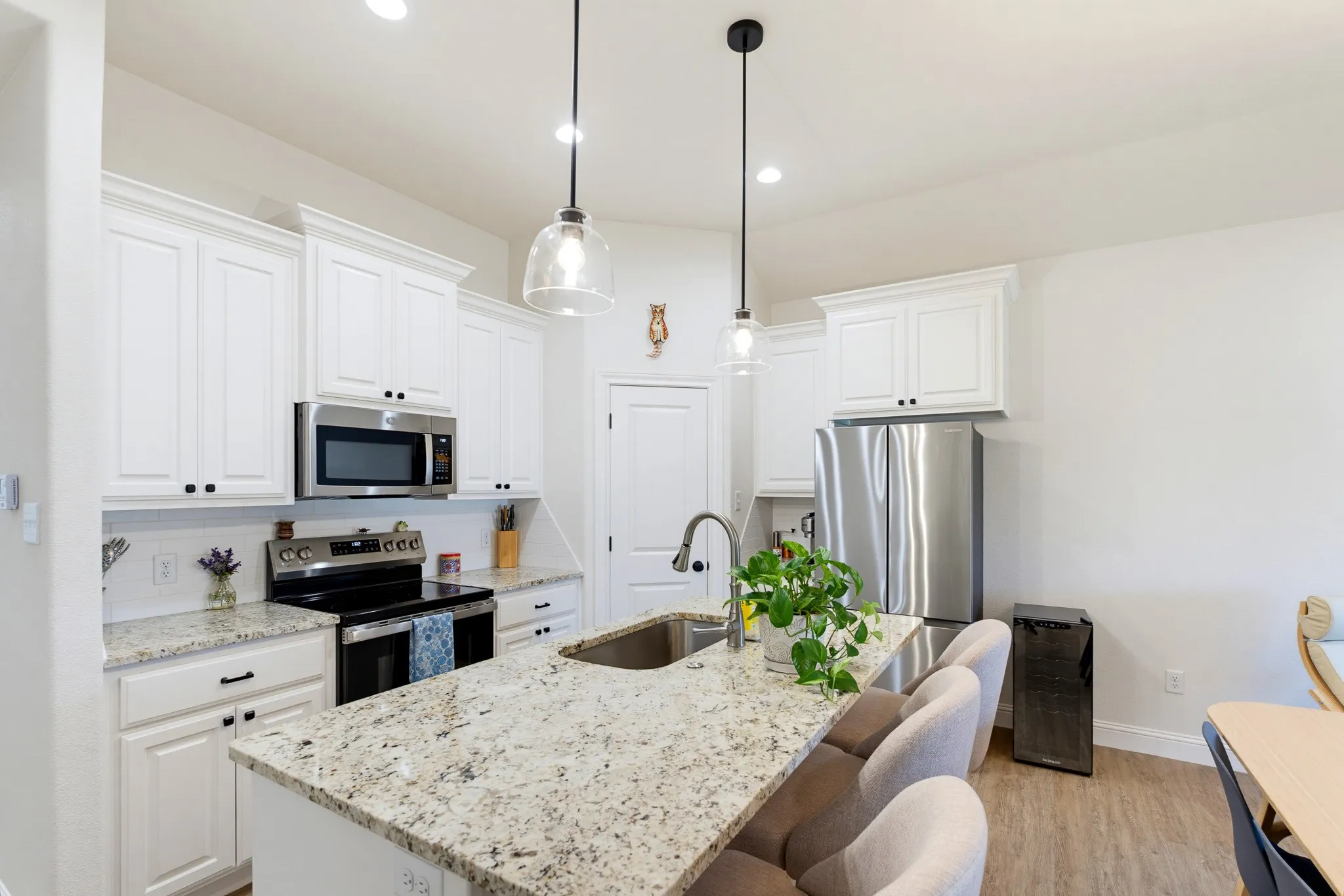 White shaker-style cabinetry with crown molding, stainless steel appliances, speckled granite countertops, a kitchen island with seating, and wood-finish flooring