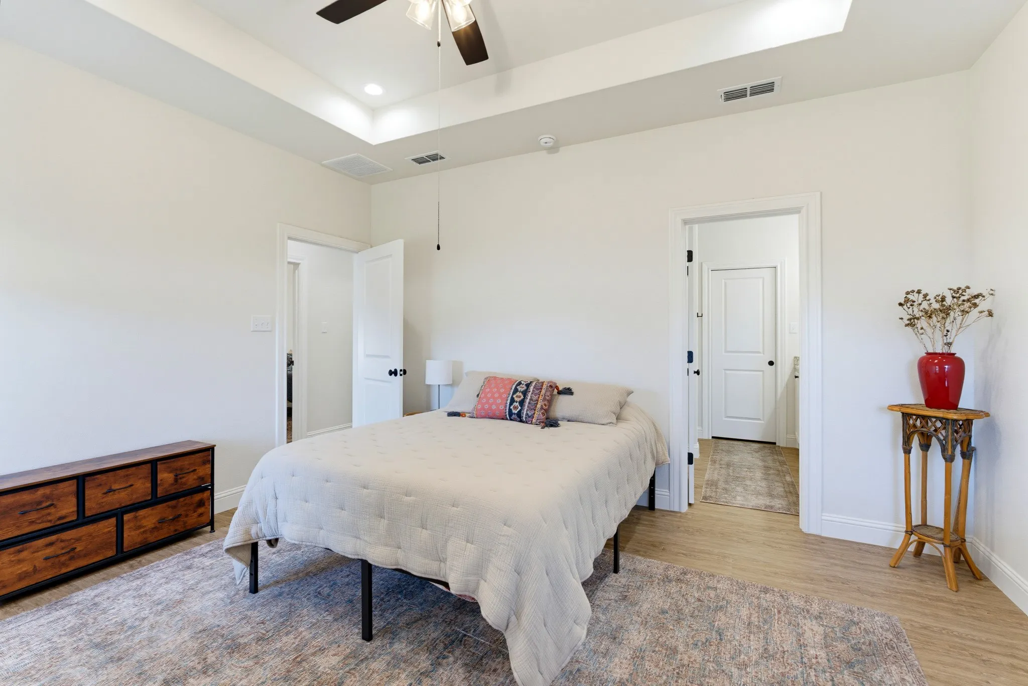Tray ceiling with recessed lighting, ceiling fan, white paneled doors, and wood-finish flooring
