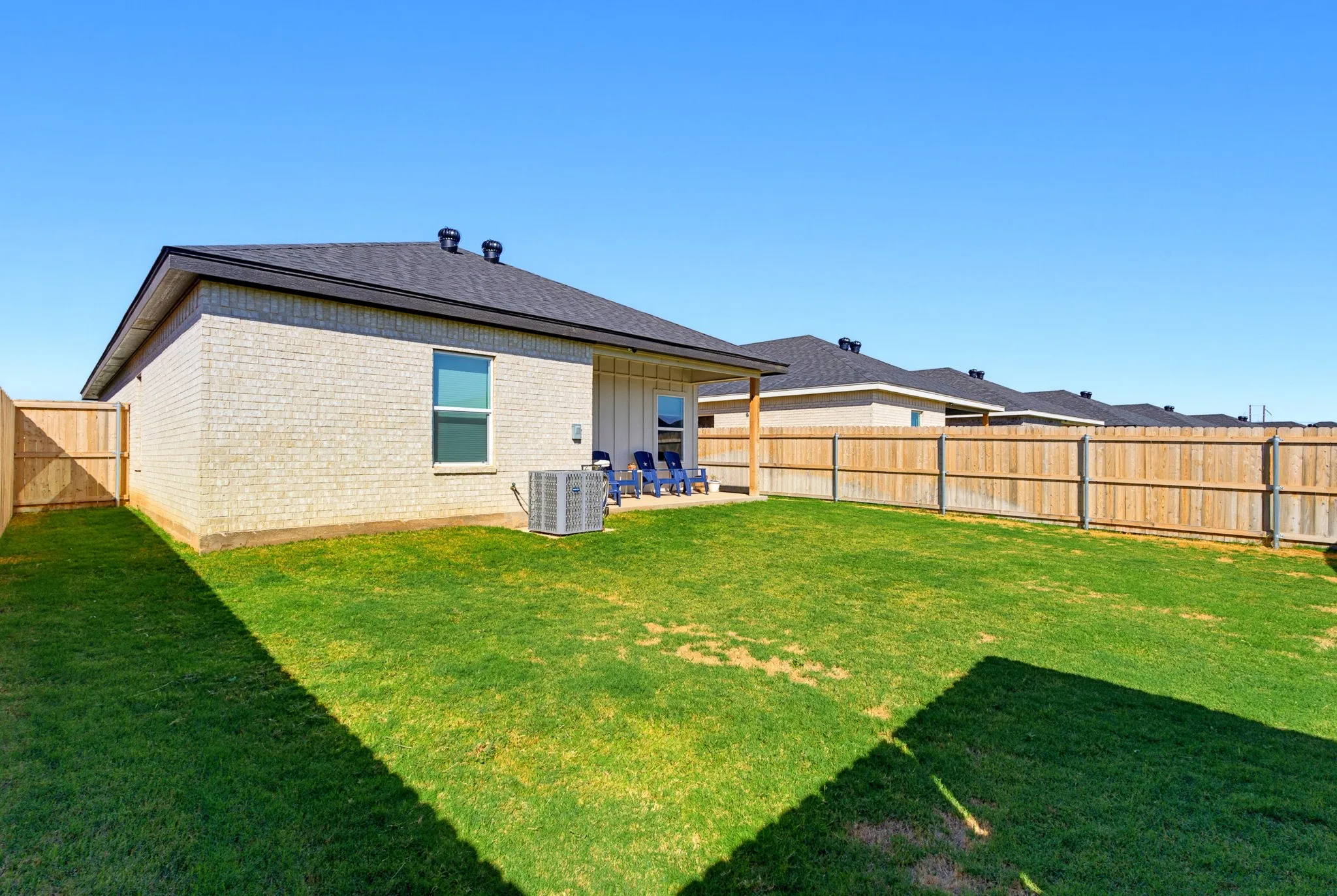 Expansive backyard featuring a manicured lawn, full perimeter wood fencing, and a light brick exterior