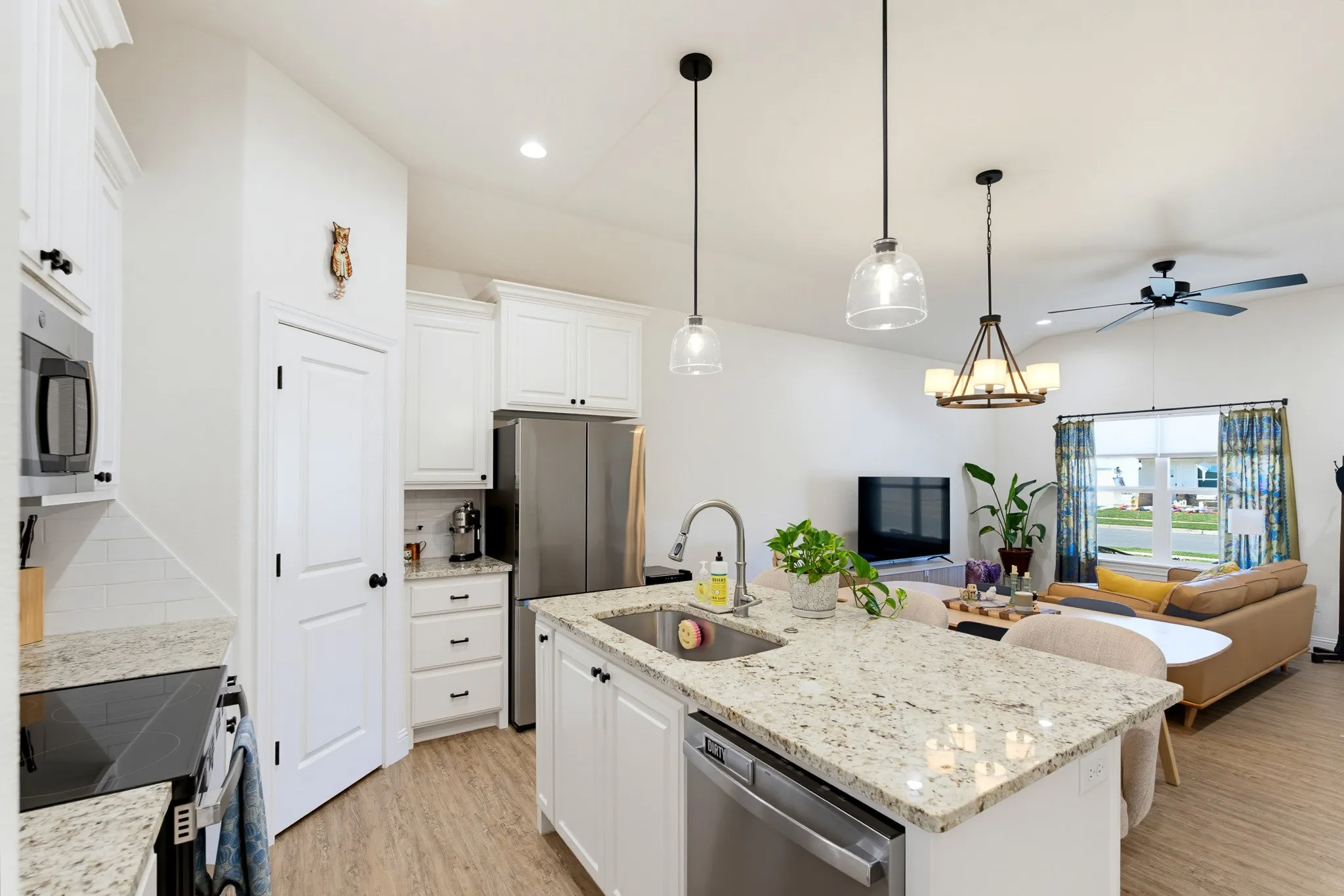 Kitchen island with integrated sink, stainless steel appliances, white cabinetry, and wood-finish flooring
