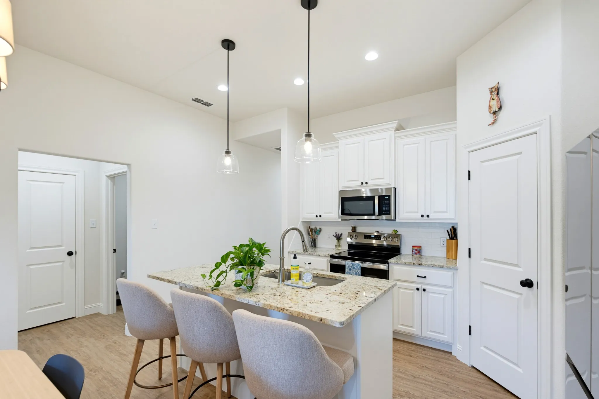 Kitchen featuring white cabinetry, stainless steel appliances, granite countertops, an island with a sink, and wood-finish flooring