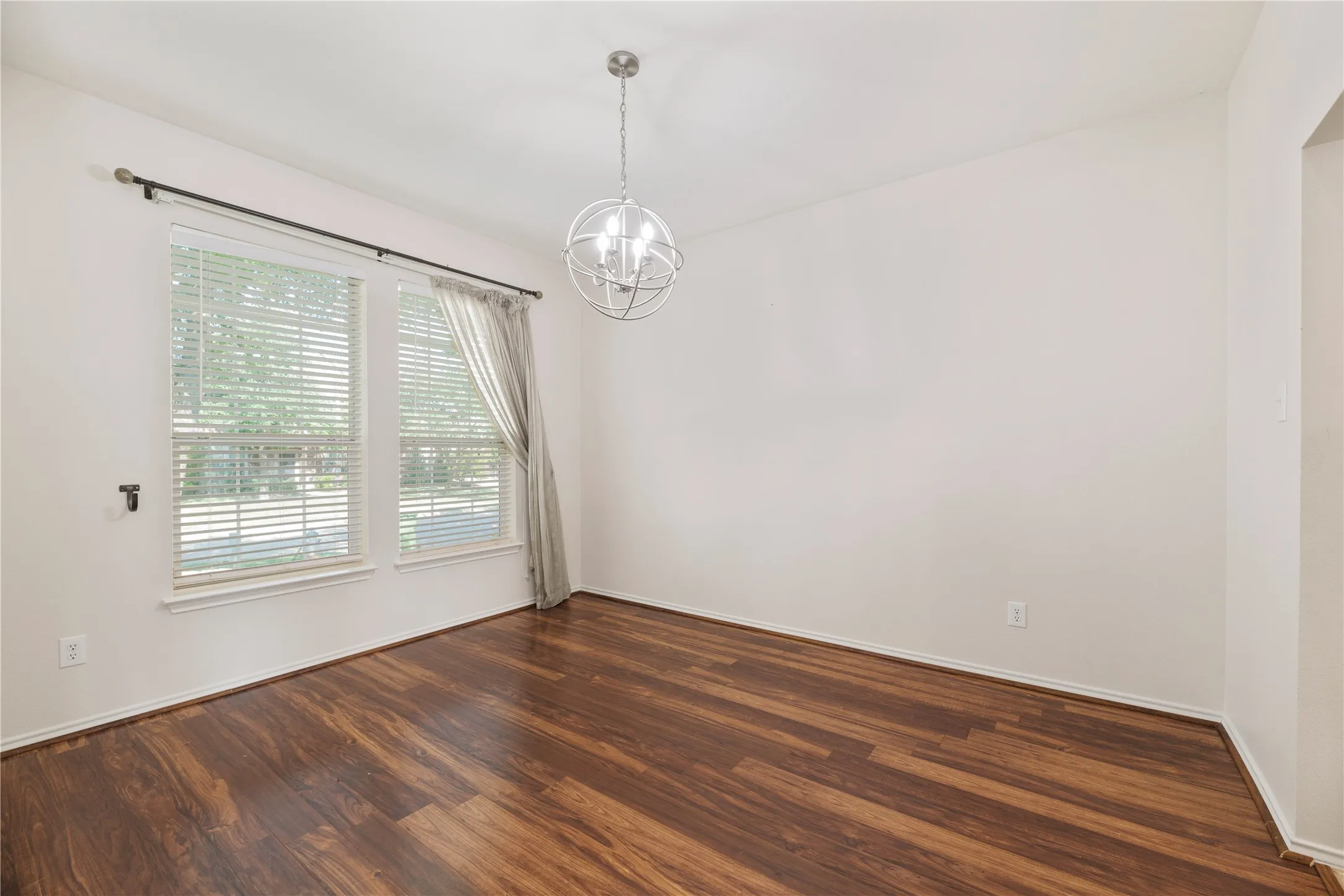 Wood-finish flooring throughout, two large windows, a contemporary spherical chandelier, and white wall finishes