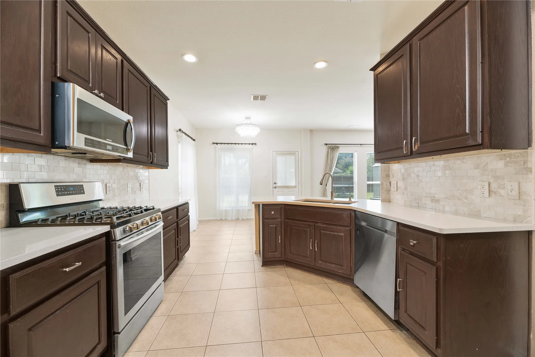 Kitchen featuring dark wood cabinetry, stainless steel appliances, light-toned countertops, tile flooring, and a tiled backsplash