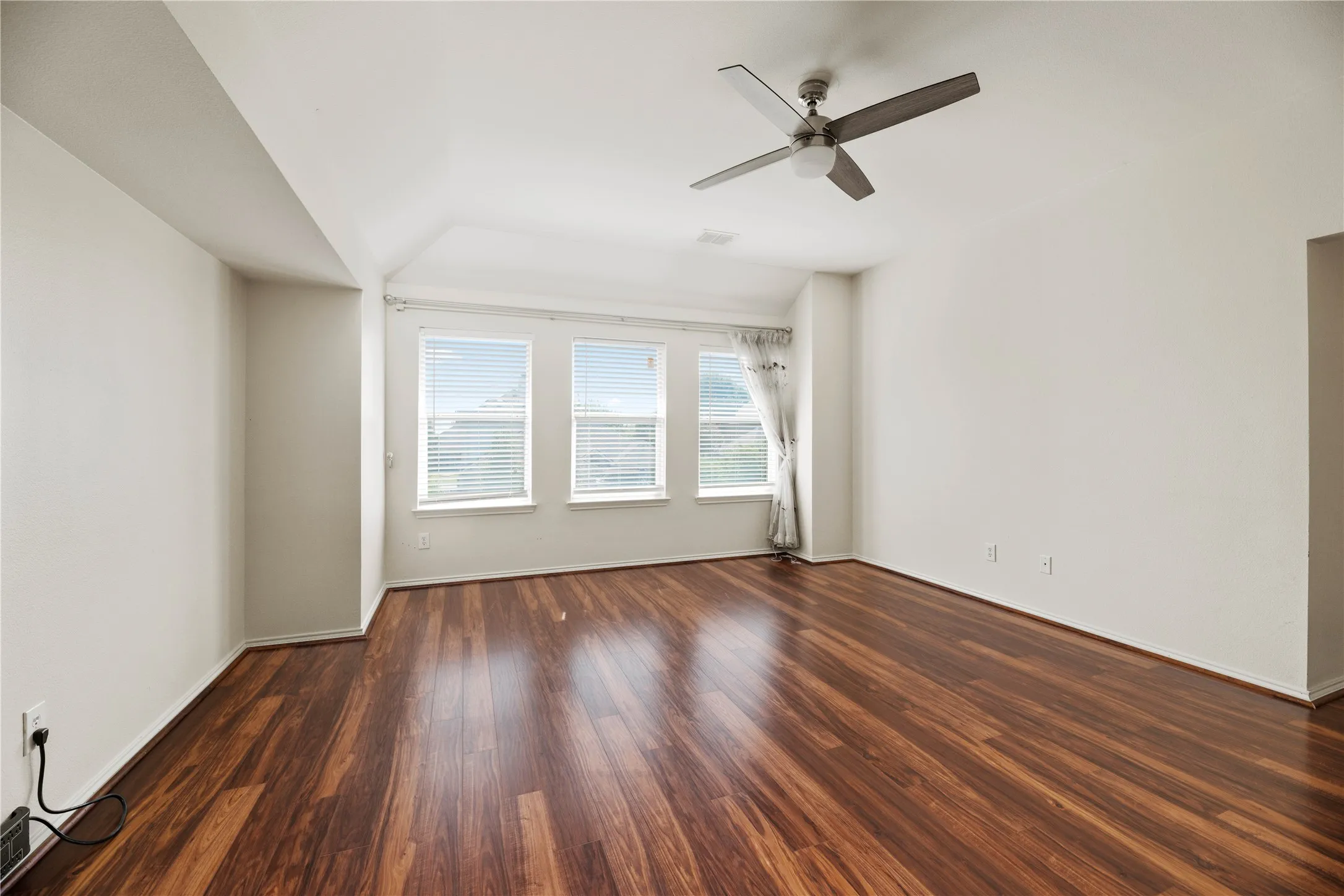 Wood-finish flooring throughout, multiple windows with blinds, and a ceiling fan with integrated lighting