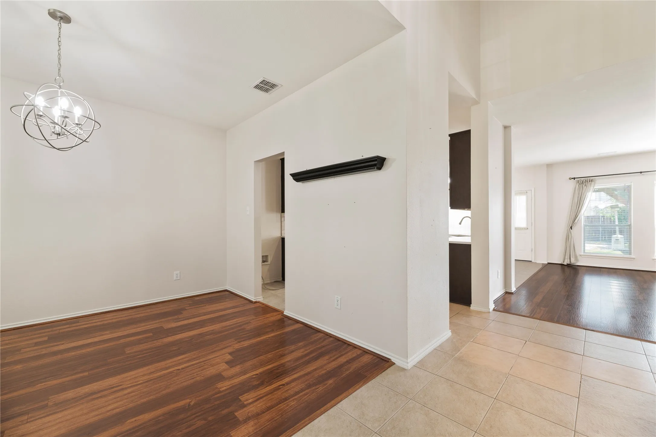 Wood-finish flooring, contemporary chandelier, tile flooring, and integrated wall shelving
