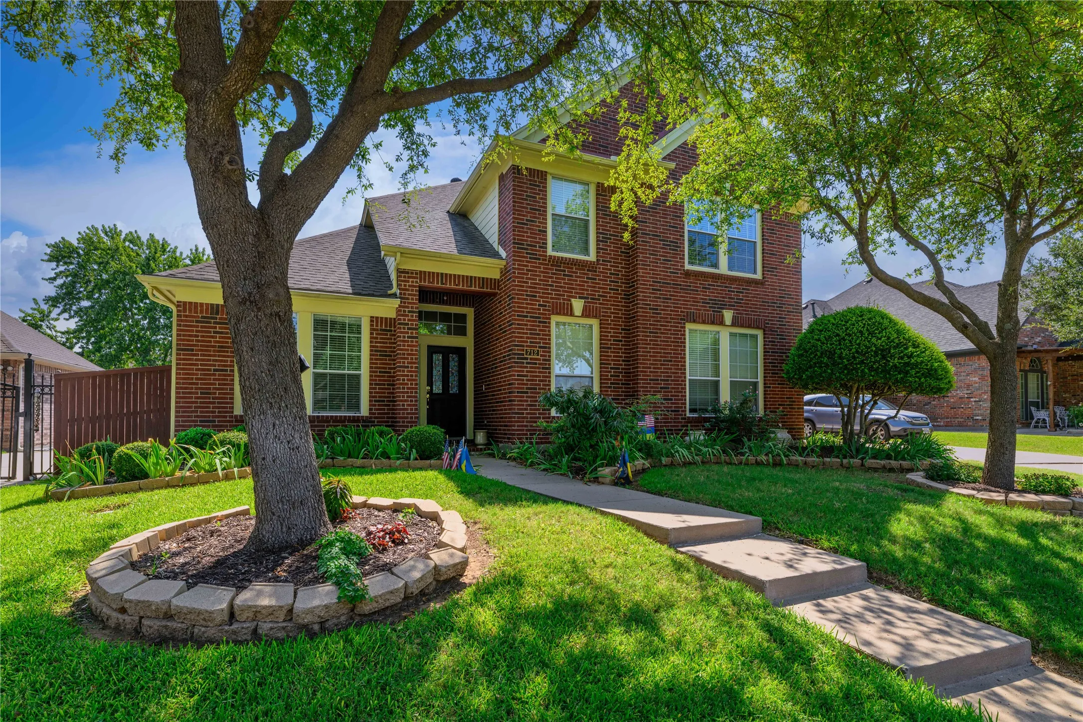 Brick exterior with light-colored trim, concrete walkway, established landscaping, and mature trees