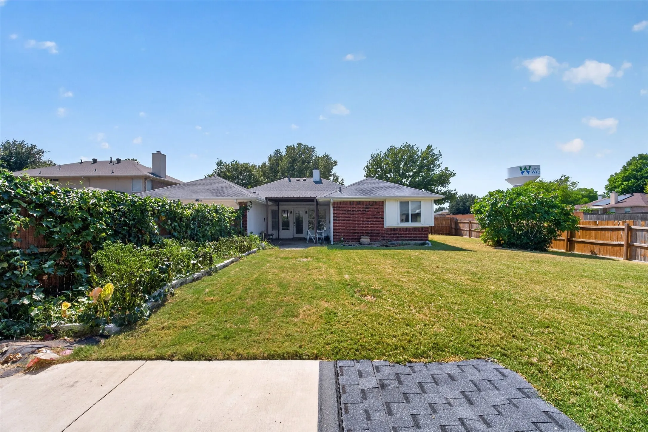 Expansive backyard featuring a lush lawn, mature perimeter landscaping, wood fencing, and a covered patio with white columns