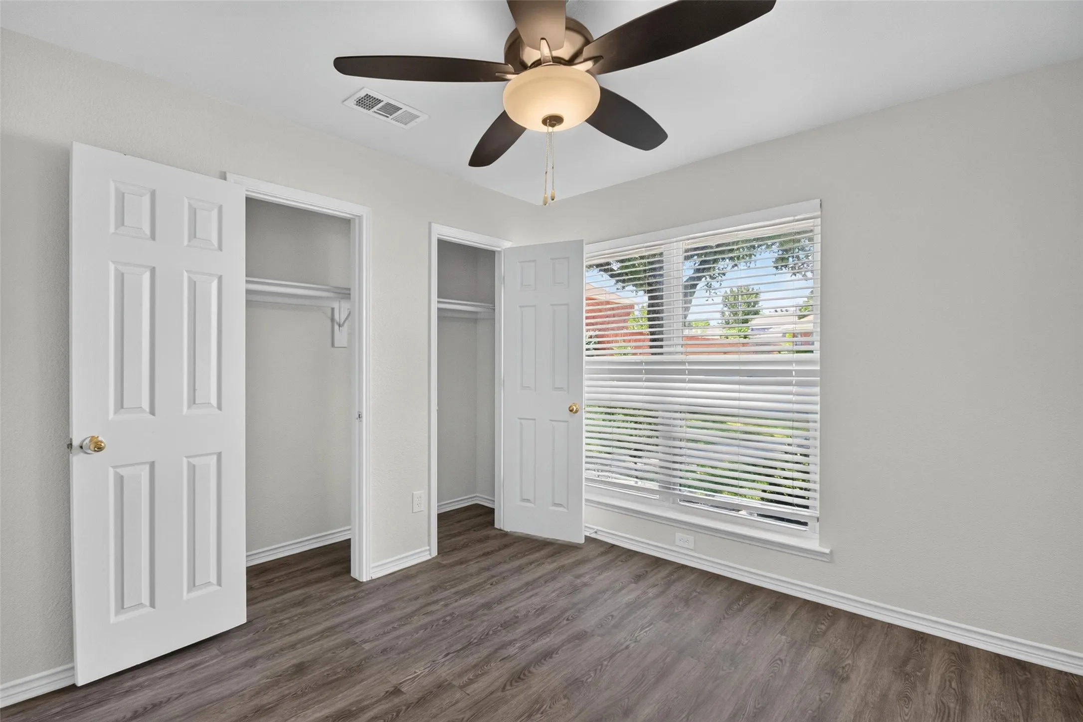 Wood-finish flooring, ceiling fan with integrated lighting, window with blinds, and dual closets with bi-fold doors