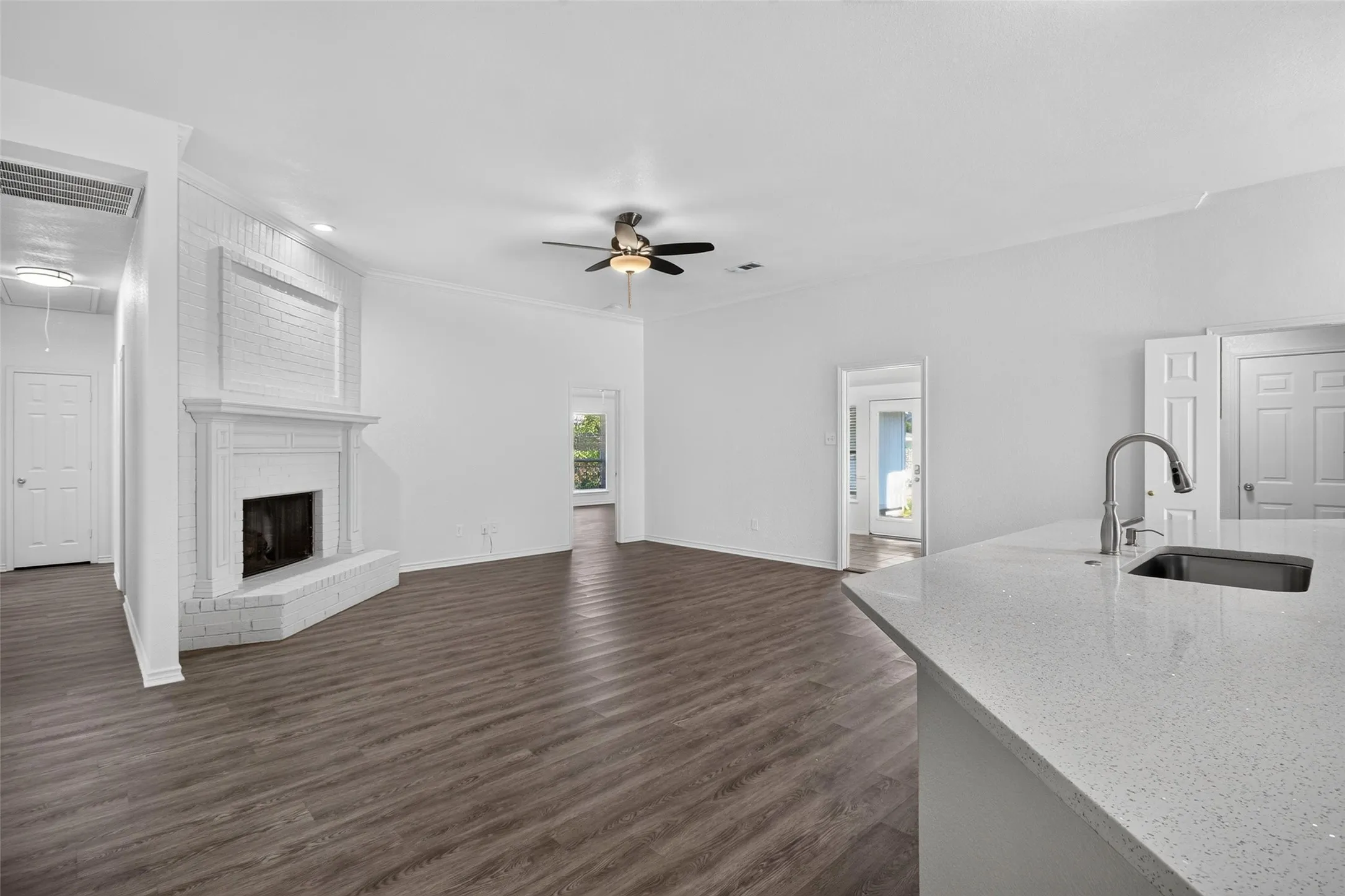 Spacious living area featuring a white brick fireplace, wood-finish flooring, and a ceiling fan