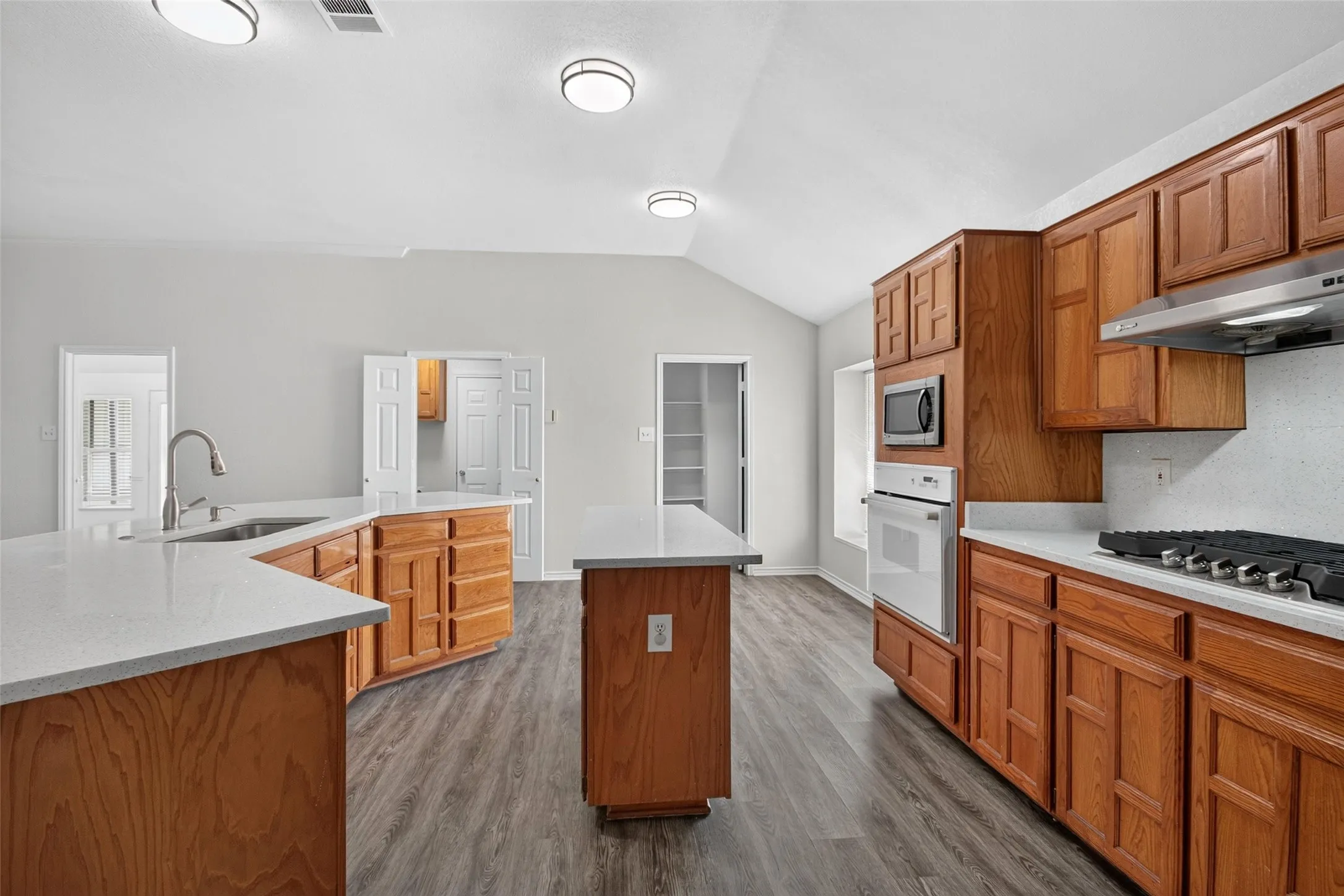 Kitchen featuring wood-finish cabinetry, light-toned countertops, a stainless steel gas range, and a built-in oven with a microwave
