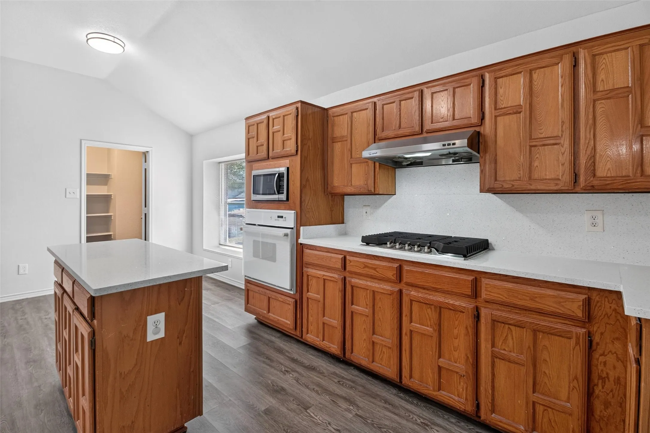 Wood-finish flooring, vaulted ceiling, and built-in white appliances