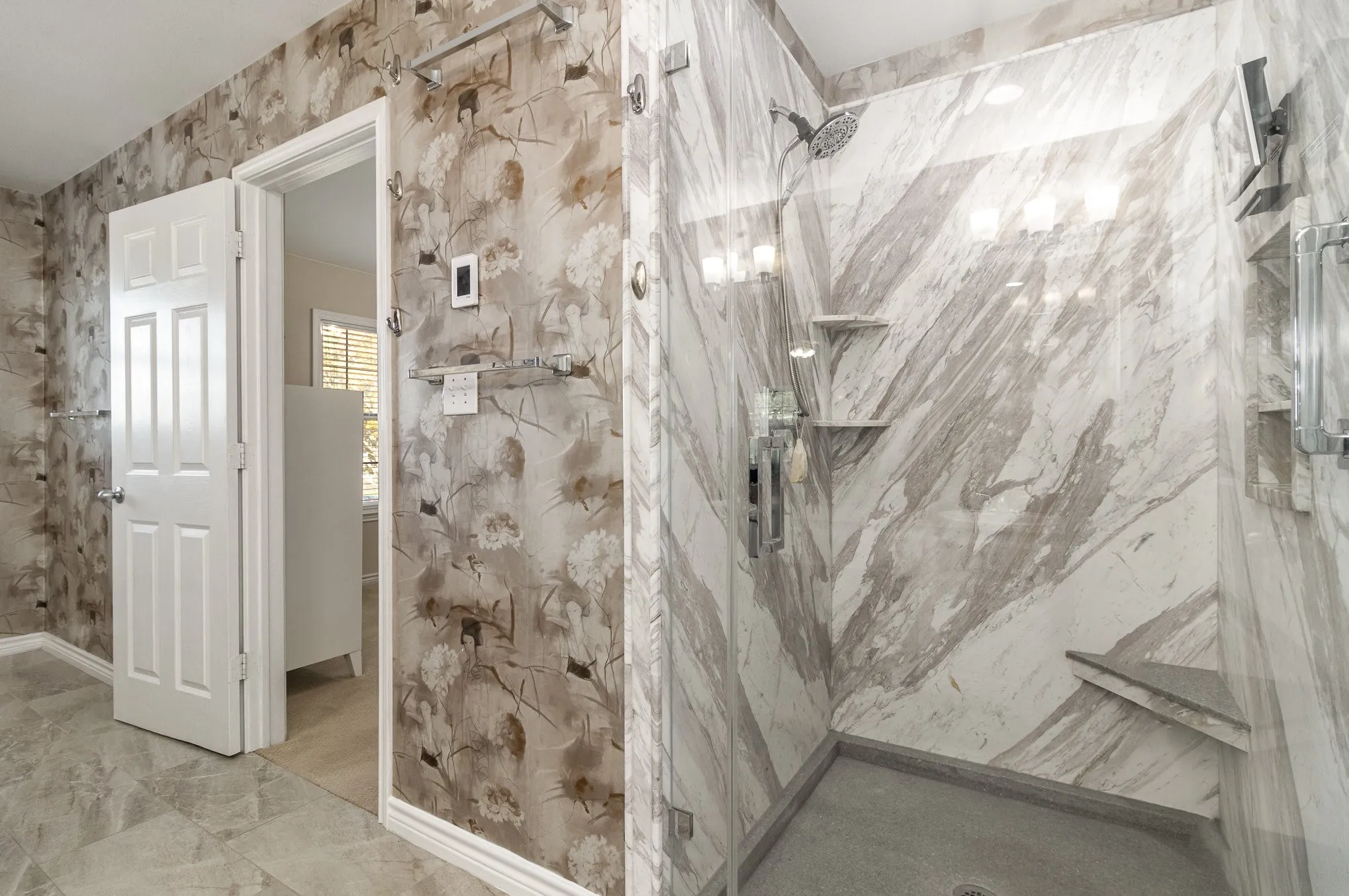 Seamless glass walk-in shower has been custom-designed with inset shelving, foot rest, additional corner shelving and magnetic rain-shower head.