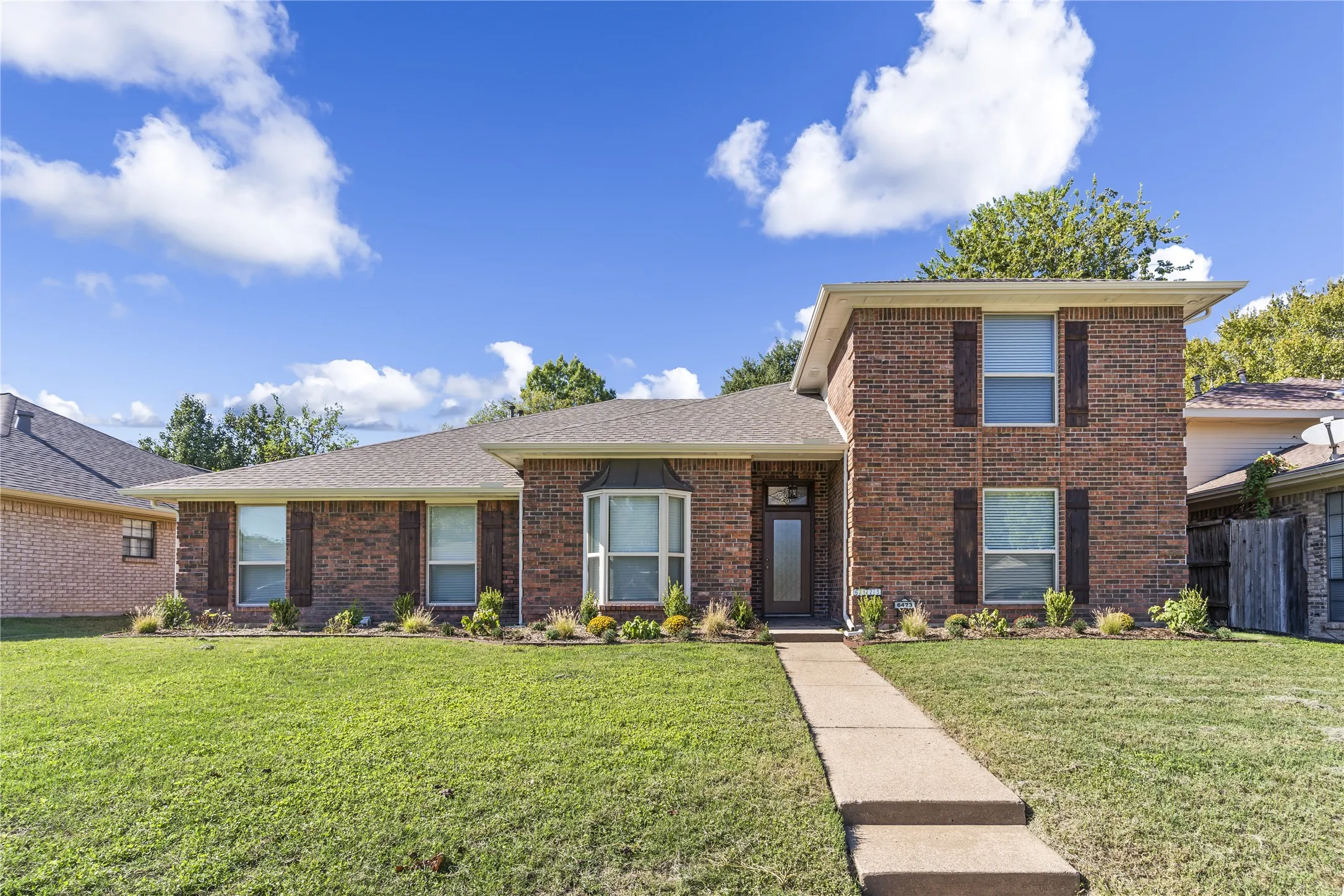 Brick exterior with brown shutters, a bay window, and a concrete walkway