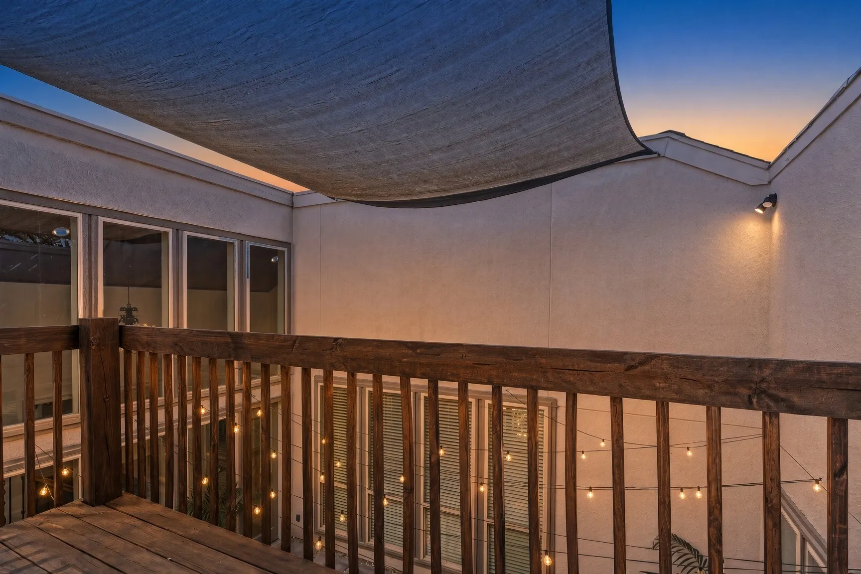 Evening on the Upper-level deck with wood railing overlook the Courtyard, protective shade covering, exterior wall lighting, and multiple windows