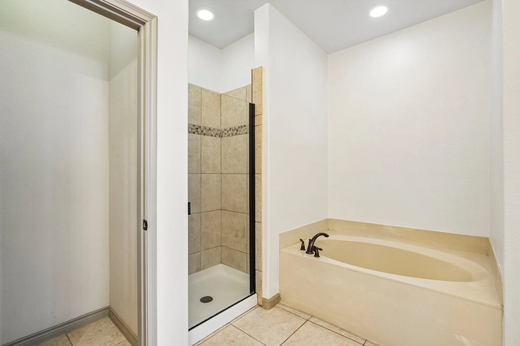 Tiled walk-in shower with a glass enclosure, separate soaking tub with bronze-finish fixtures, recessed lighting, and tile flooring