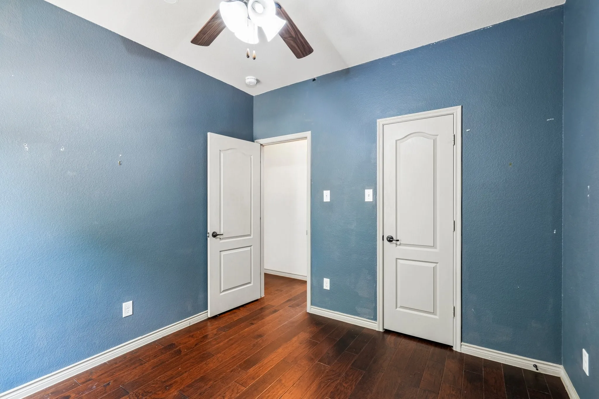 Wood-finish flooring, white panel doors, and a ceiling fan with integrated lighting