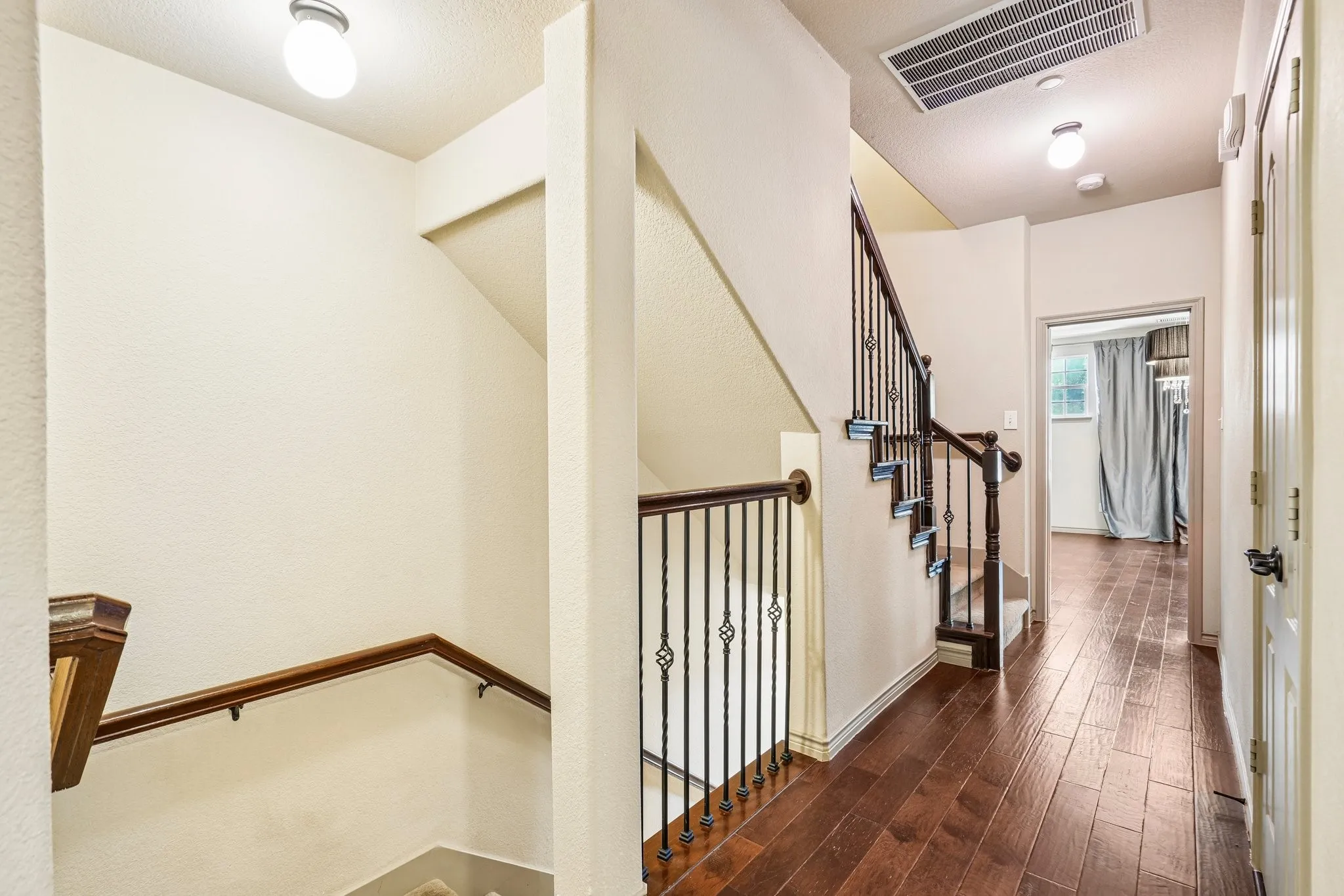 Hardwood-style flooring throughout the hallway and room, staircase with wrought iron balusters, and a rich wood-finish handrail