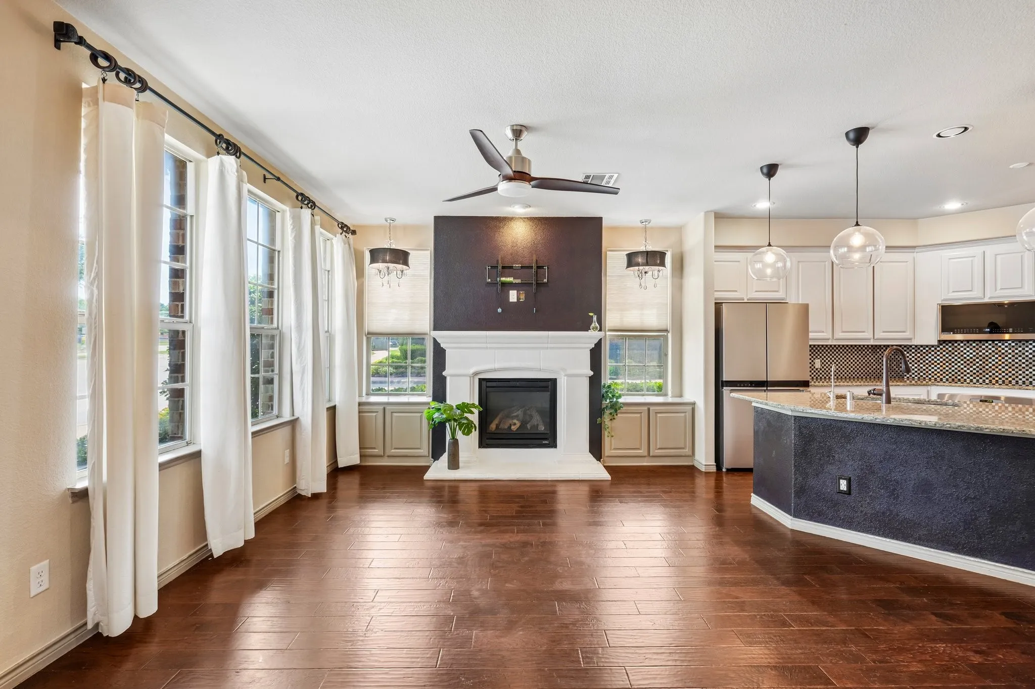 Wood-finish flooring, white mantel fireplace, stainless steel appliances, white cabinetry, and a kitchen island with pendant lighting