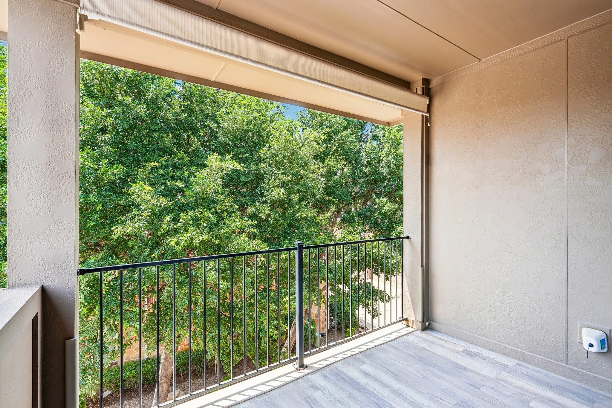 Outdoor balcony featuring wood-finish flooring, a black metal railing, and a retractable awning