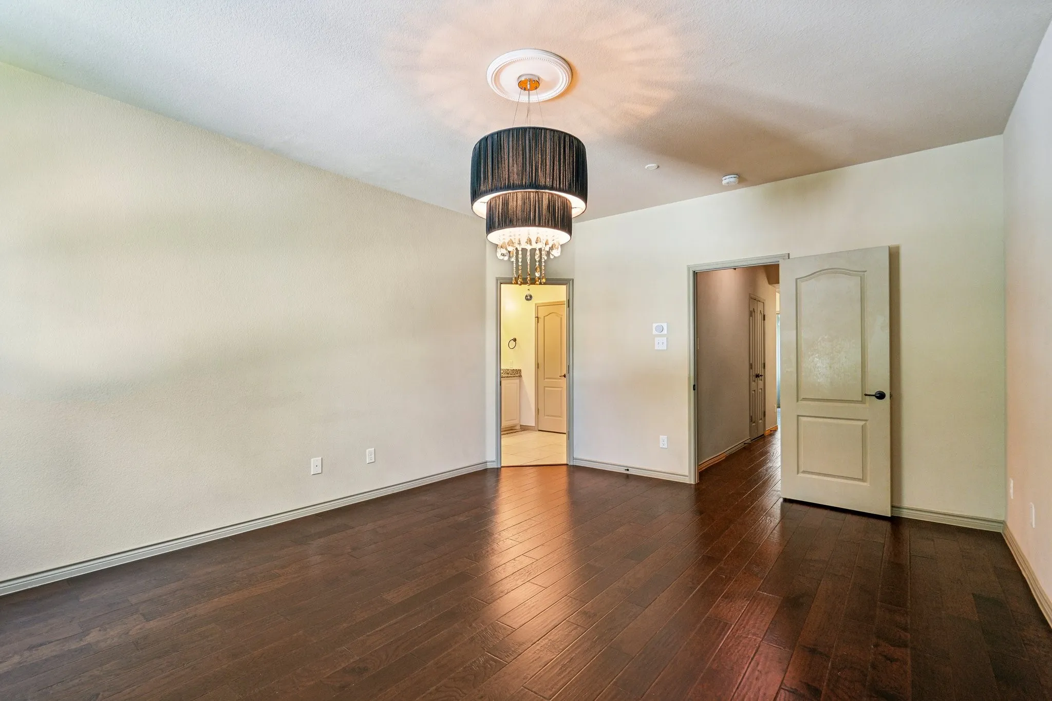 Dark wood-finish flooring, light neutral-toned walls, and a tiered chandelier with crystal accents