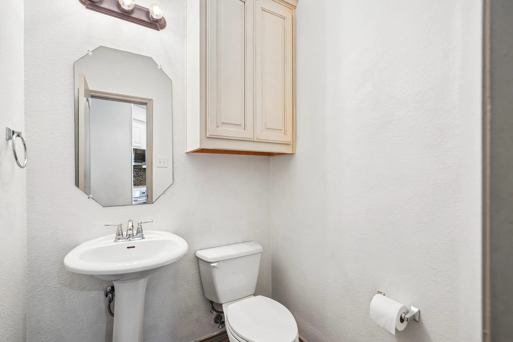 Pedestal sink with chrome faucet, octagonal mirror, built-in cabinetry, and wall-mounted light fixture