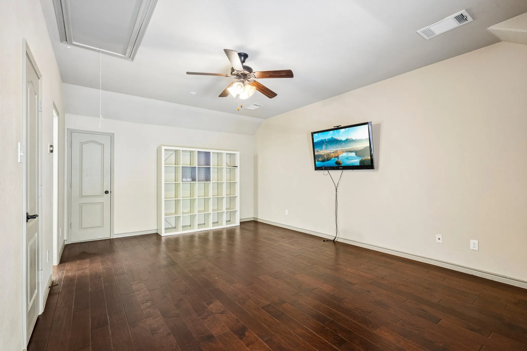 Wood-finish flooring throughout, ceiling fan with integrated lighting, and white built-in shelving unit