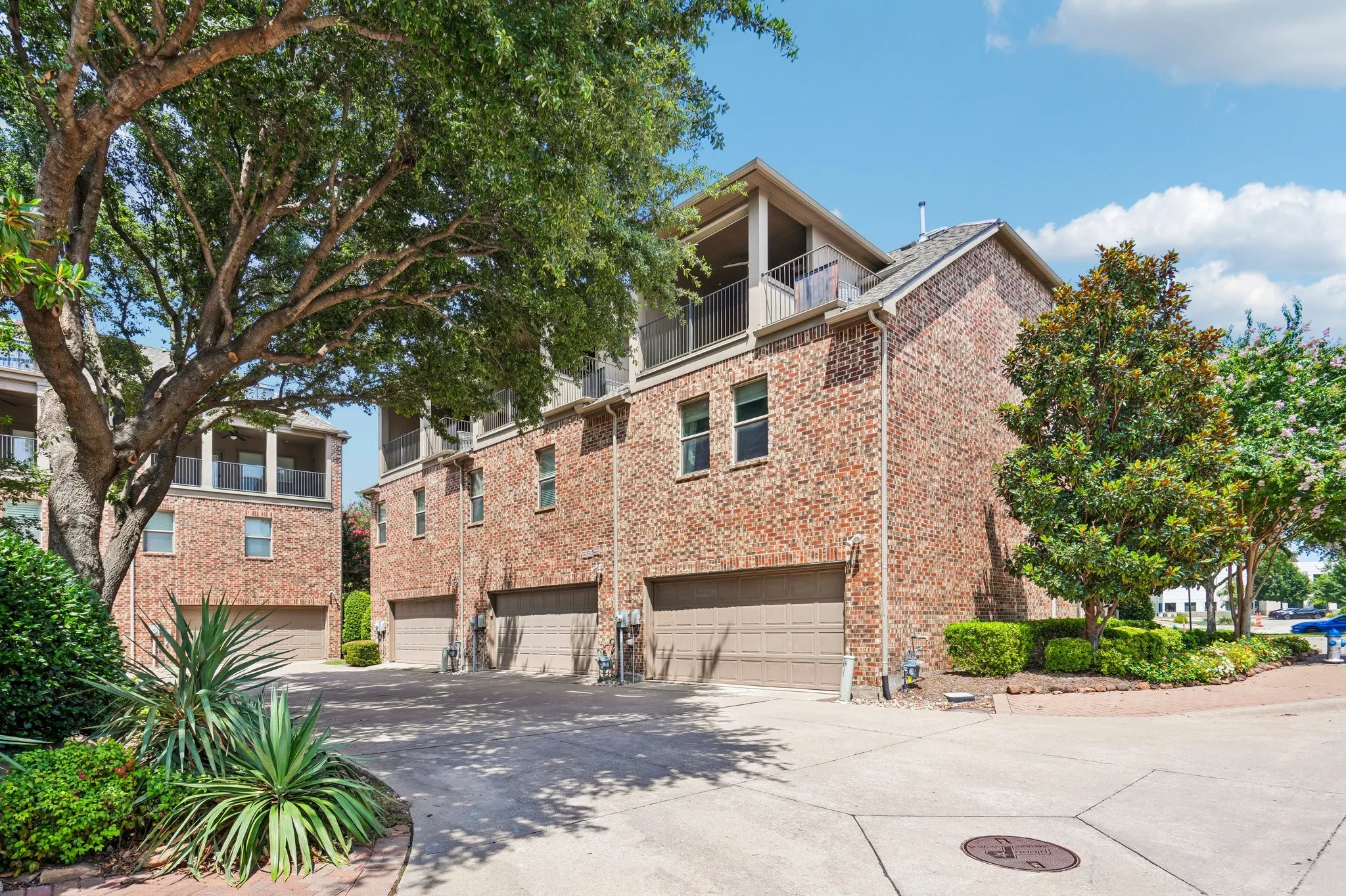 Brick exterior facade, multiple attached garages, upper-level balconies, mature trees, and landscaped shrubbery