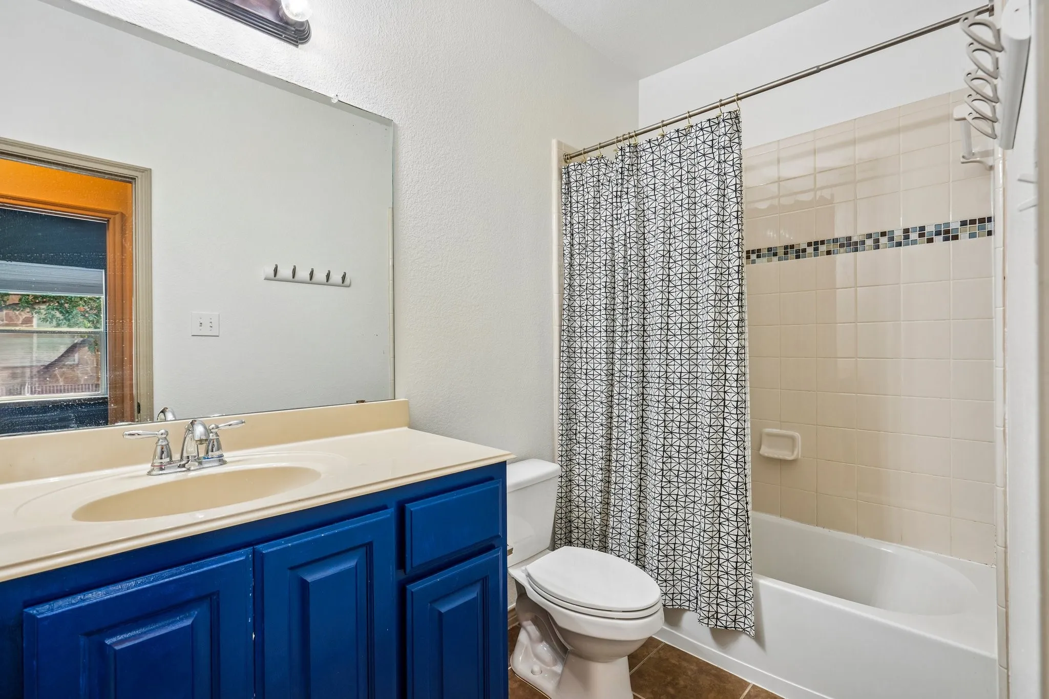 Vanity with integrated sink, vibrant blue cabinetry, large wall mirror, and a tiled shower-tub combination with decorative accent band