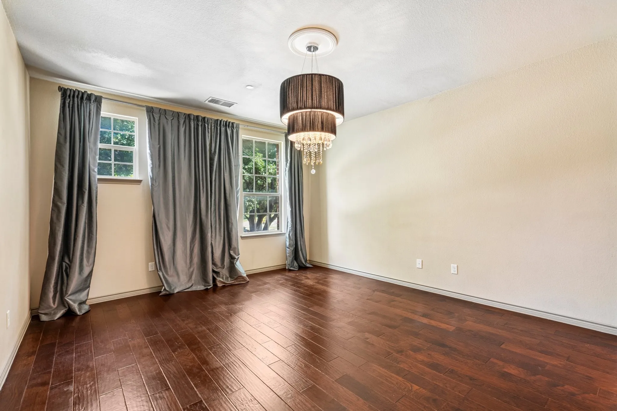 Hardwood flooring, two windows with grid patterns, and a tiered chandelier