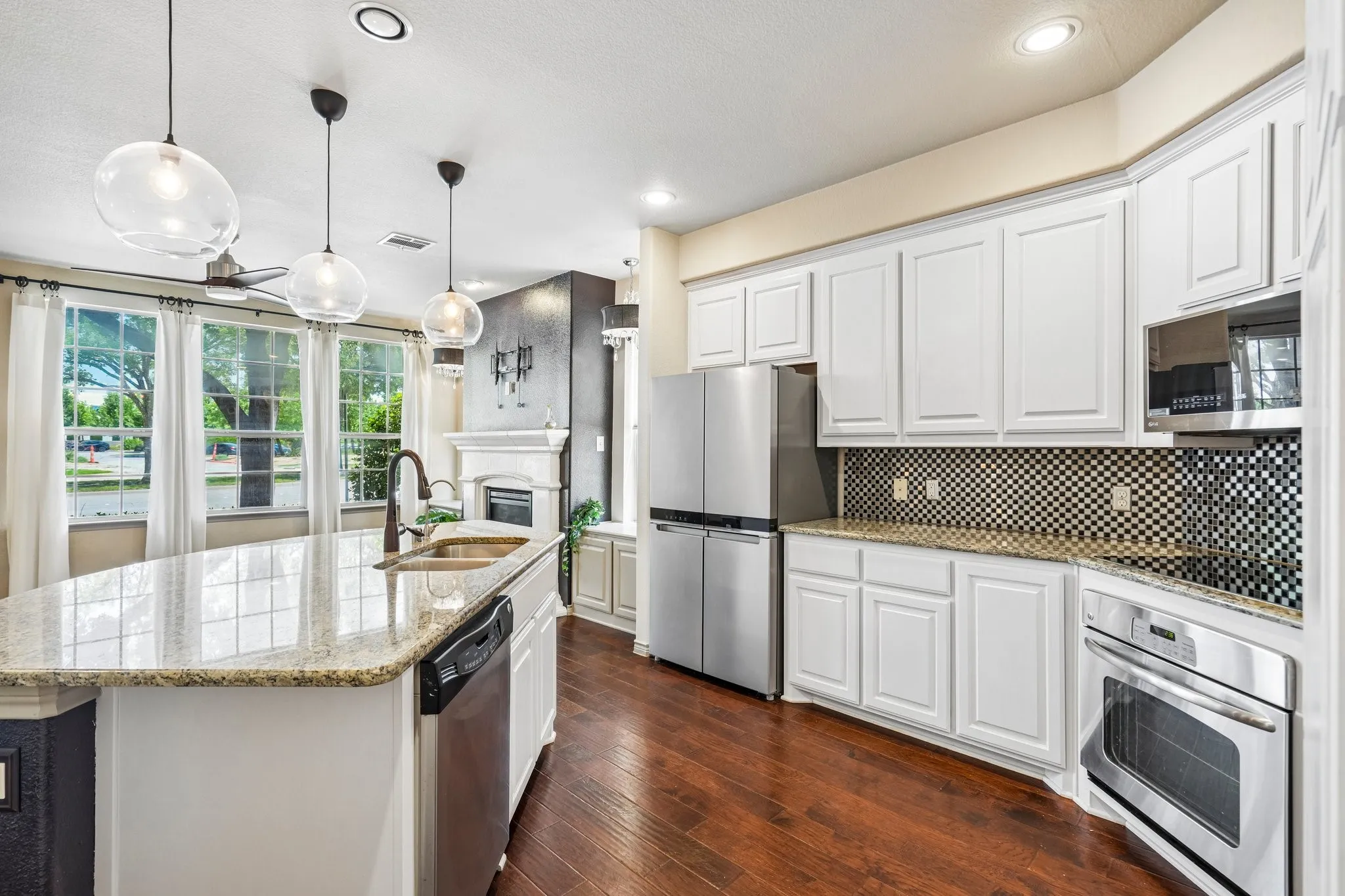 Kitchen featuring a large central island with granite countertops, stainless steel appliances, white cabinetry, and wood-finish flooring
