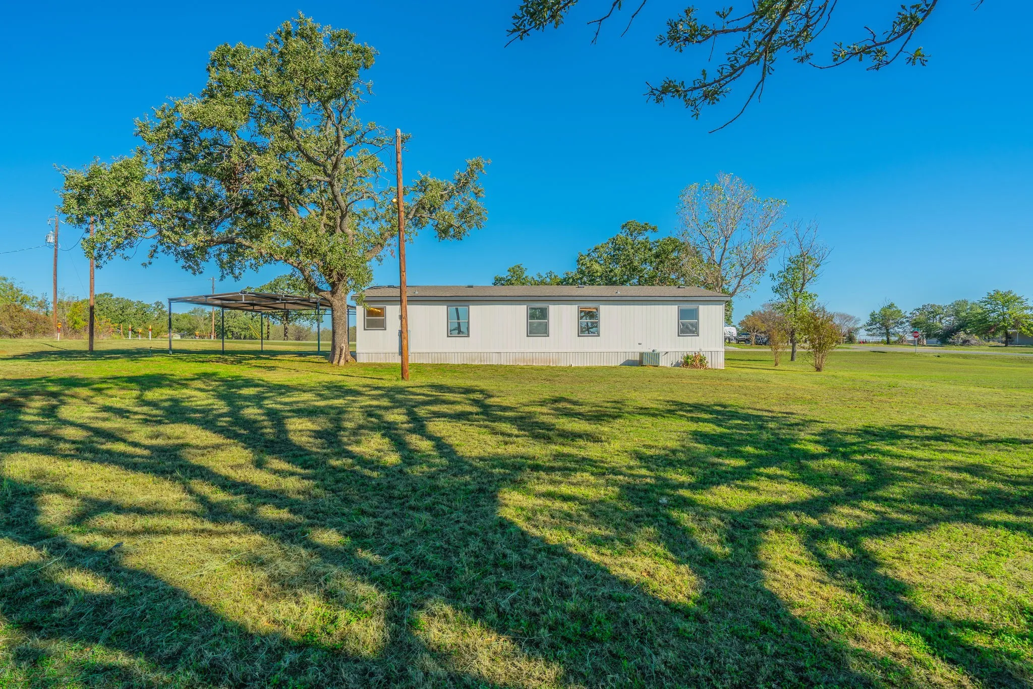 Side Exterior: Full-length view of the home showcasing multiple windows, mature shade trees, and a spacious grassy setting.