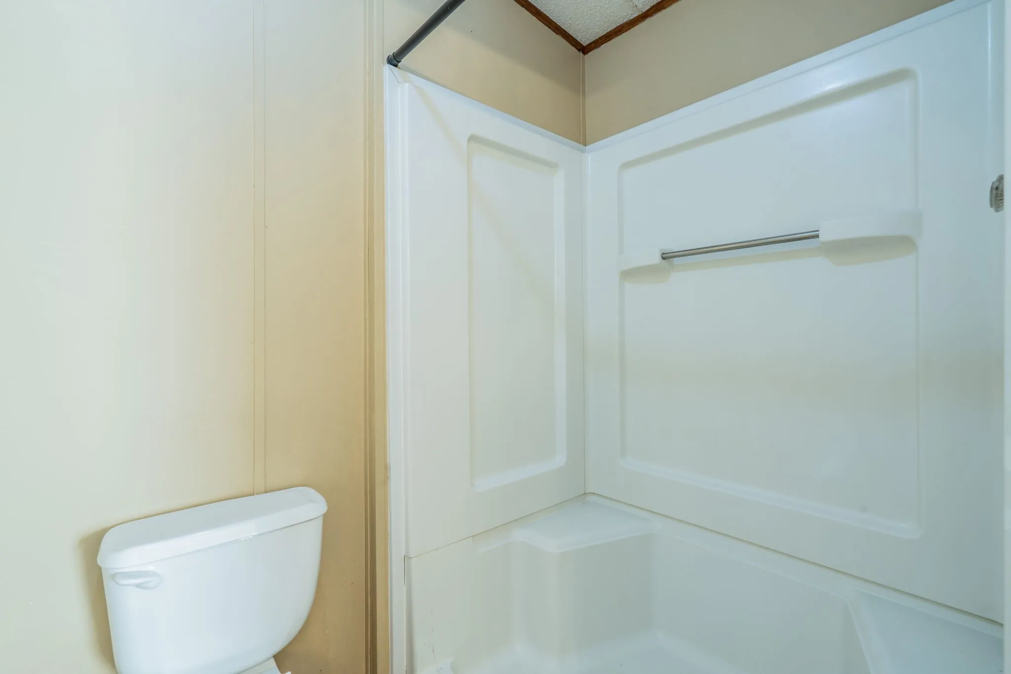 Bathroom: White tub and shower combination with molded wall surround, integrated storage ledge, and shower curtain rod.