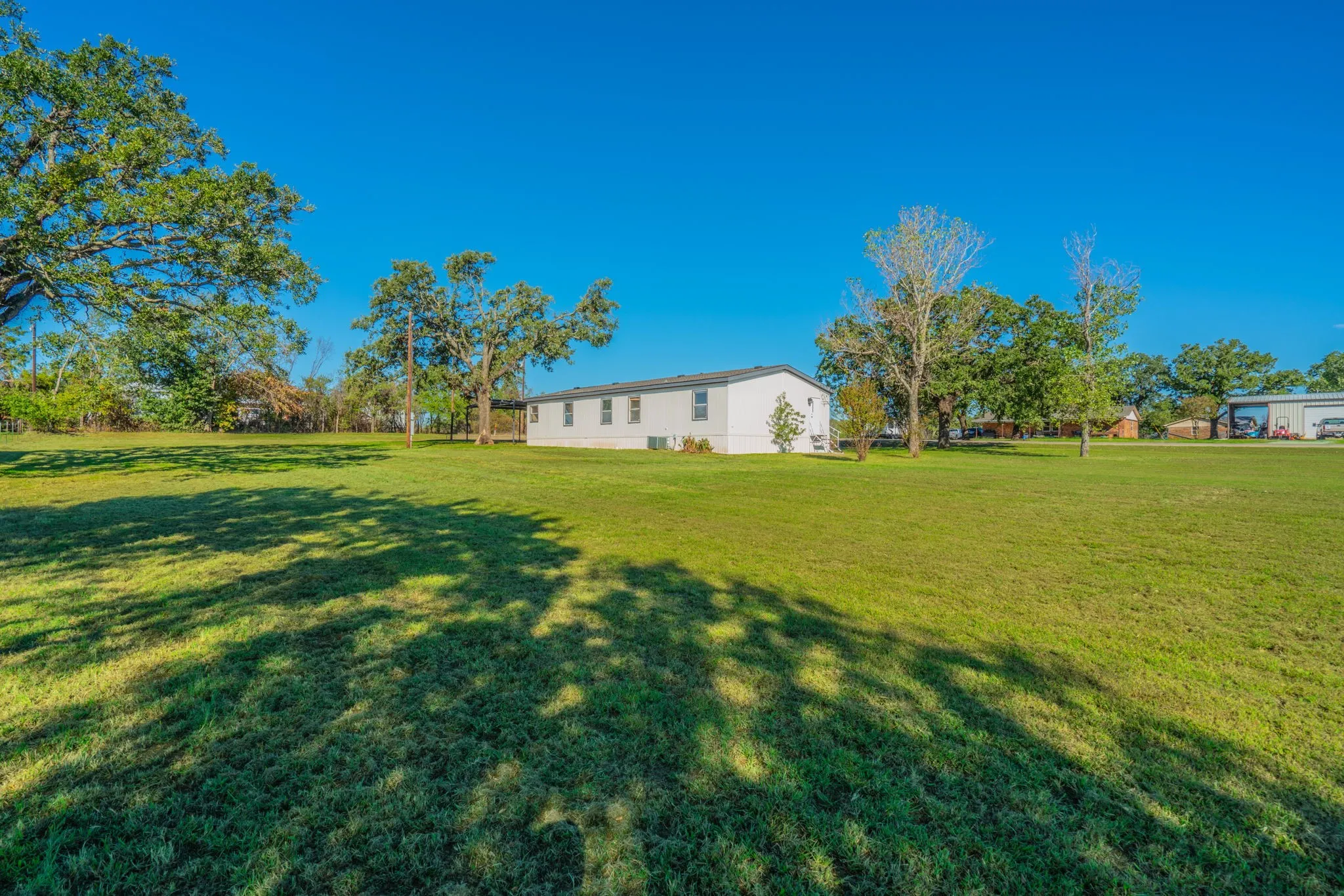 Property Grounds: Broad view of the open lawn, established trees, and home positioned within the landscaped surroundings.