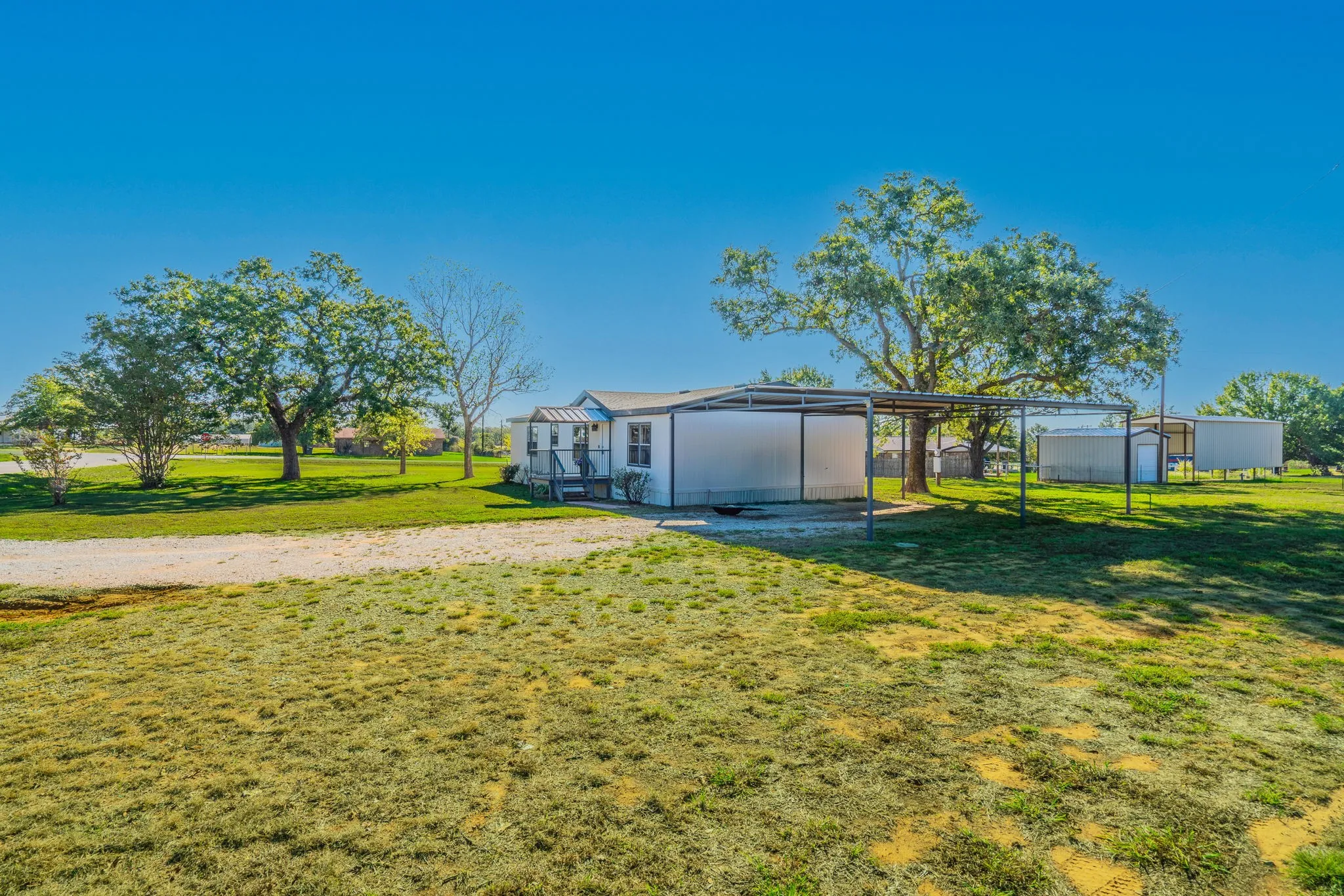 Exterior and Carport: Side view of the home featuring a metal-roofed carport, gravel driveway, and surrounding open lawn.