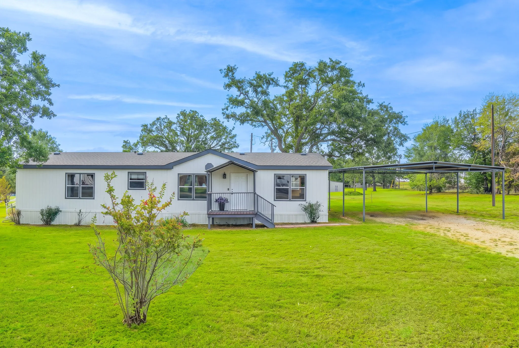 Front Exterior: Single-story home situated on a spacious, tree-lined lot featuring a covered front entry and two-vehicle metal carport.