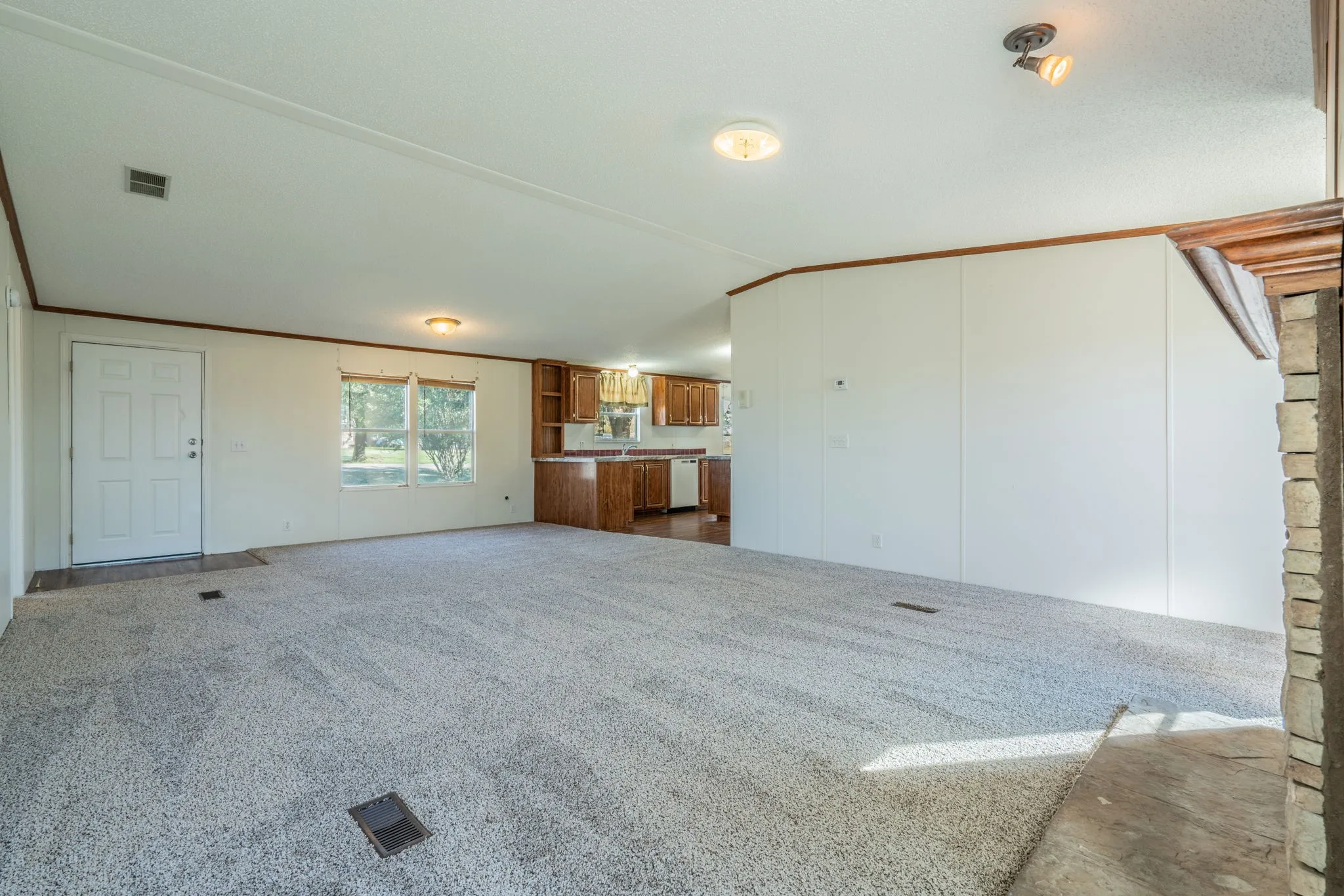 Living Room: Expansive carpeted living area with neutral walls, natural light, and an open connection to the kitchen.