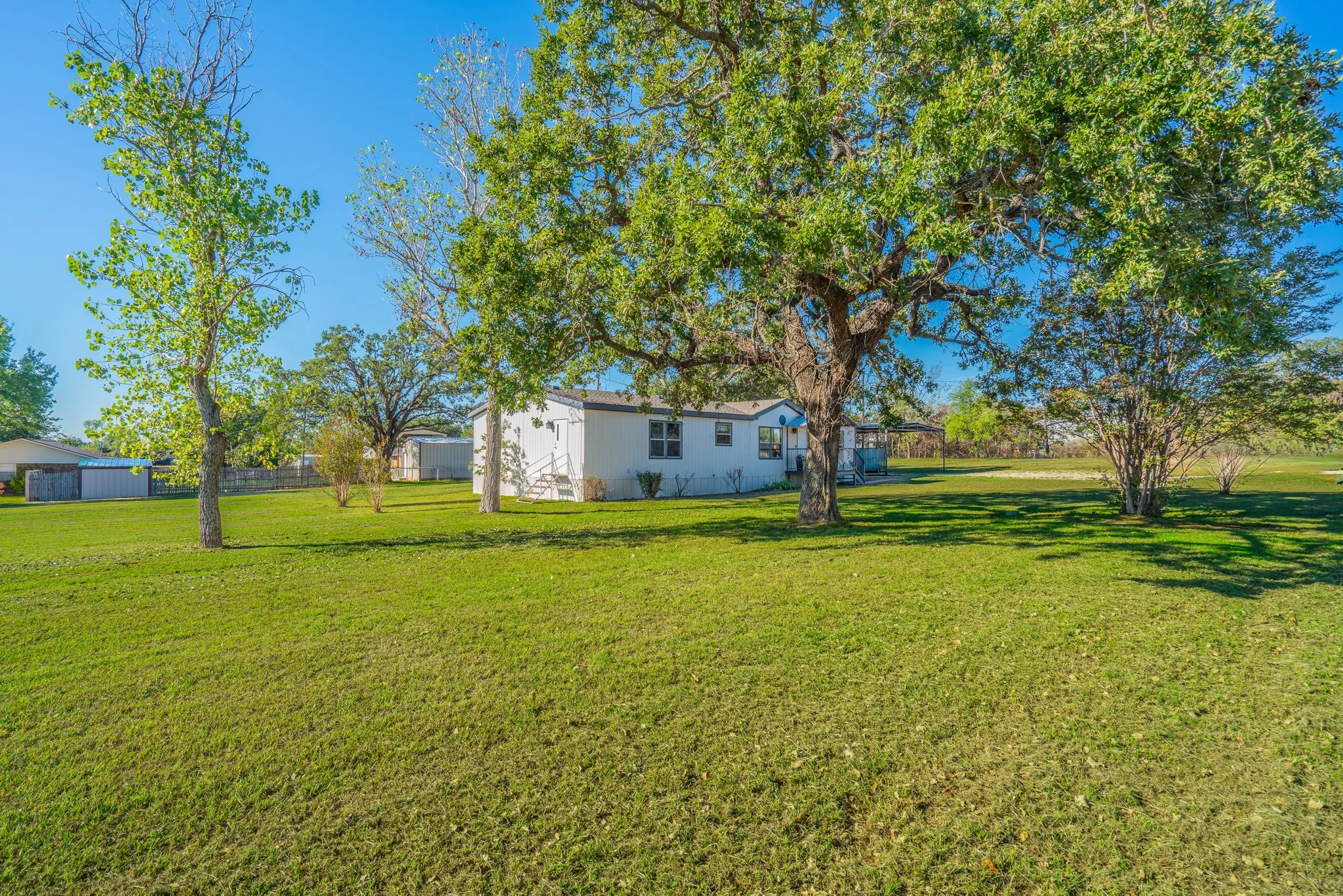 Exterior Grounds: Expansive grassy yard with mature shade trees and a wide view of the home's exterior.