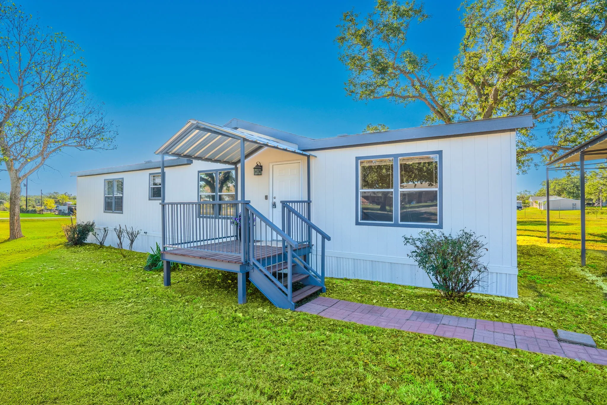 Front Entry: Welcoming covered entry featuring a metal awning, raised porch with steps and railings, and a walkway bordered by lawn.
