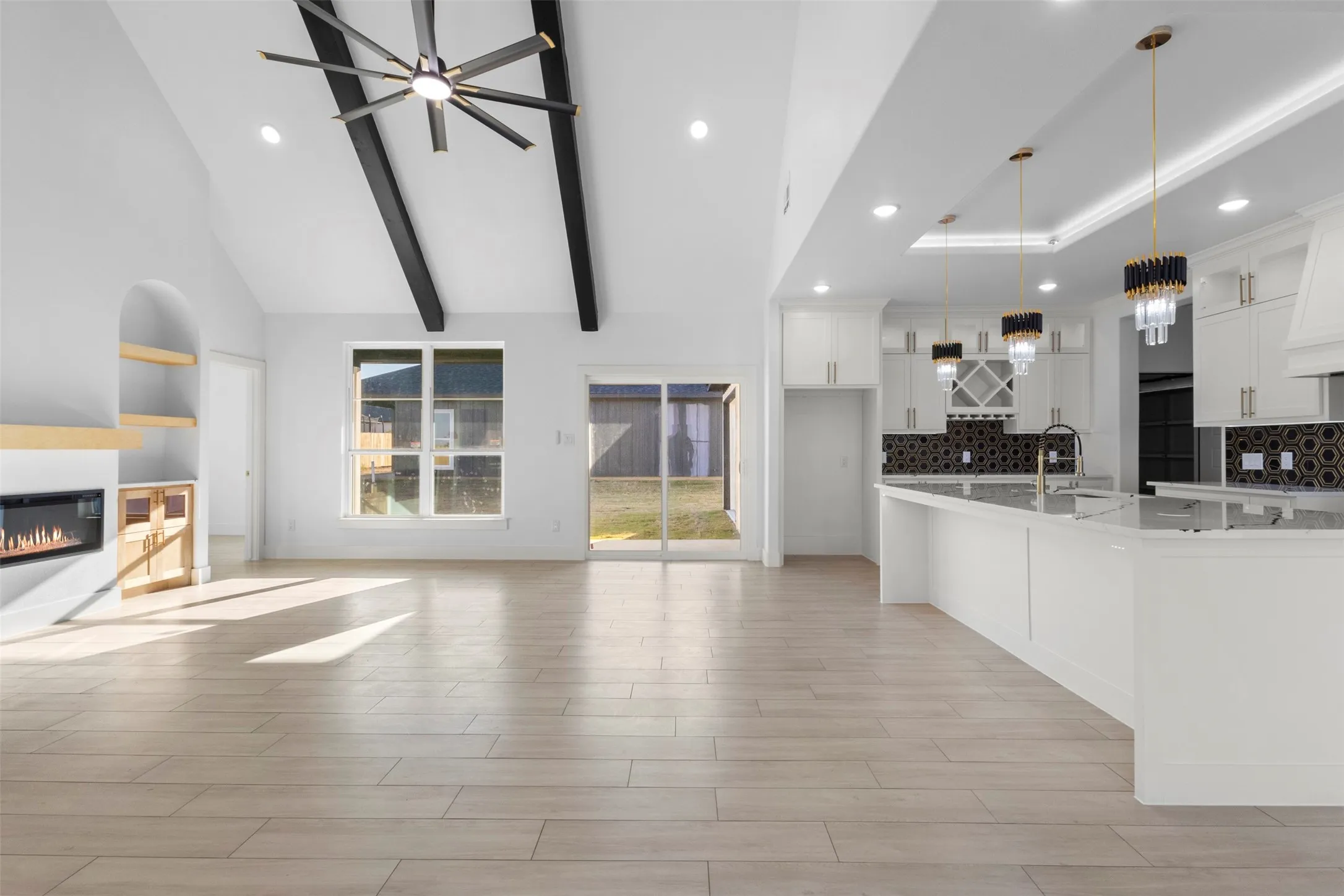 Vaulted ceilings with exposed beams, wood-finish flooring, built-in fireplace, and a kitchen featuring white cabinetry, an island, and decorative pendant lighting