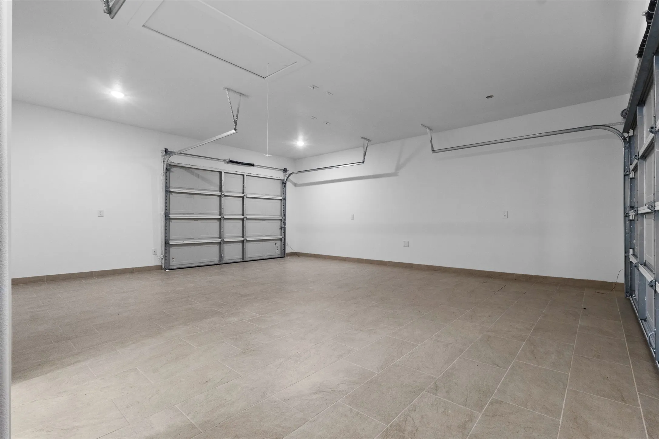 Spacious garage featuring tiled flooring, recessed lighting, and two overhead doors with tracks