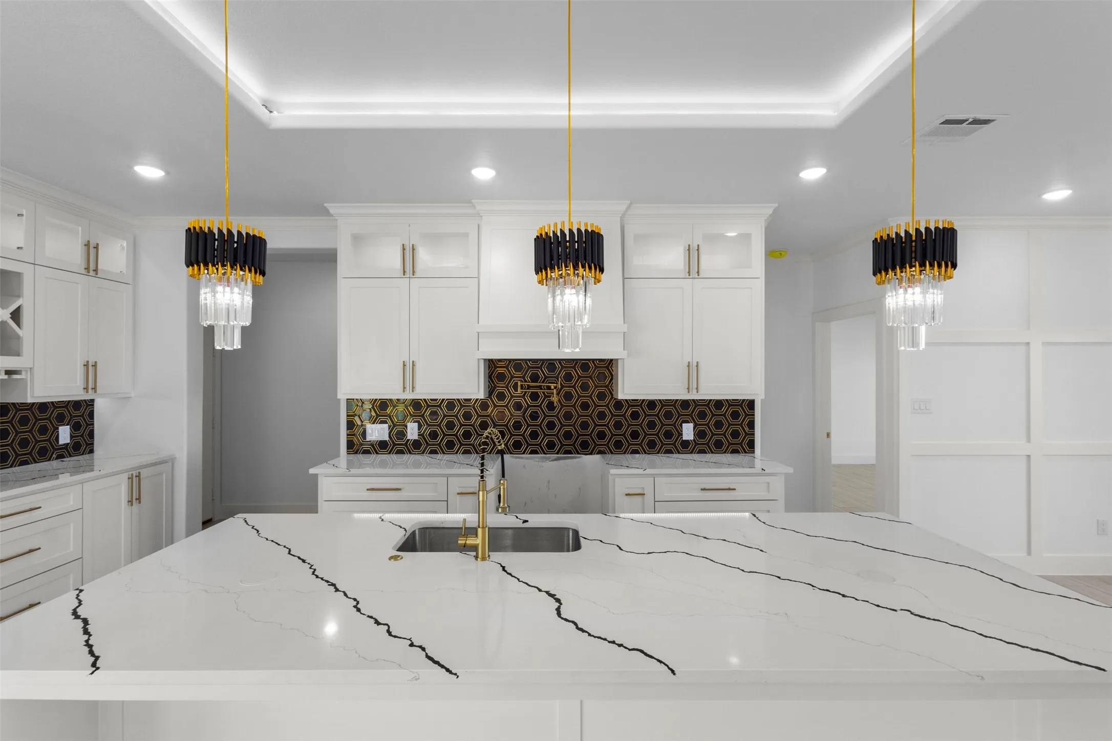 Kitchen featuring a large island with a countertop, gold-finish faucet, and three decorative pendant lights