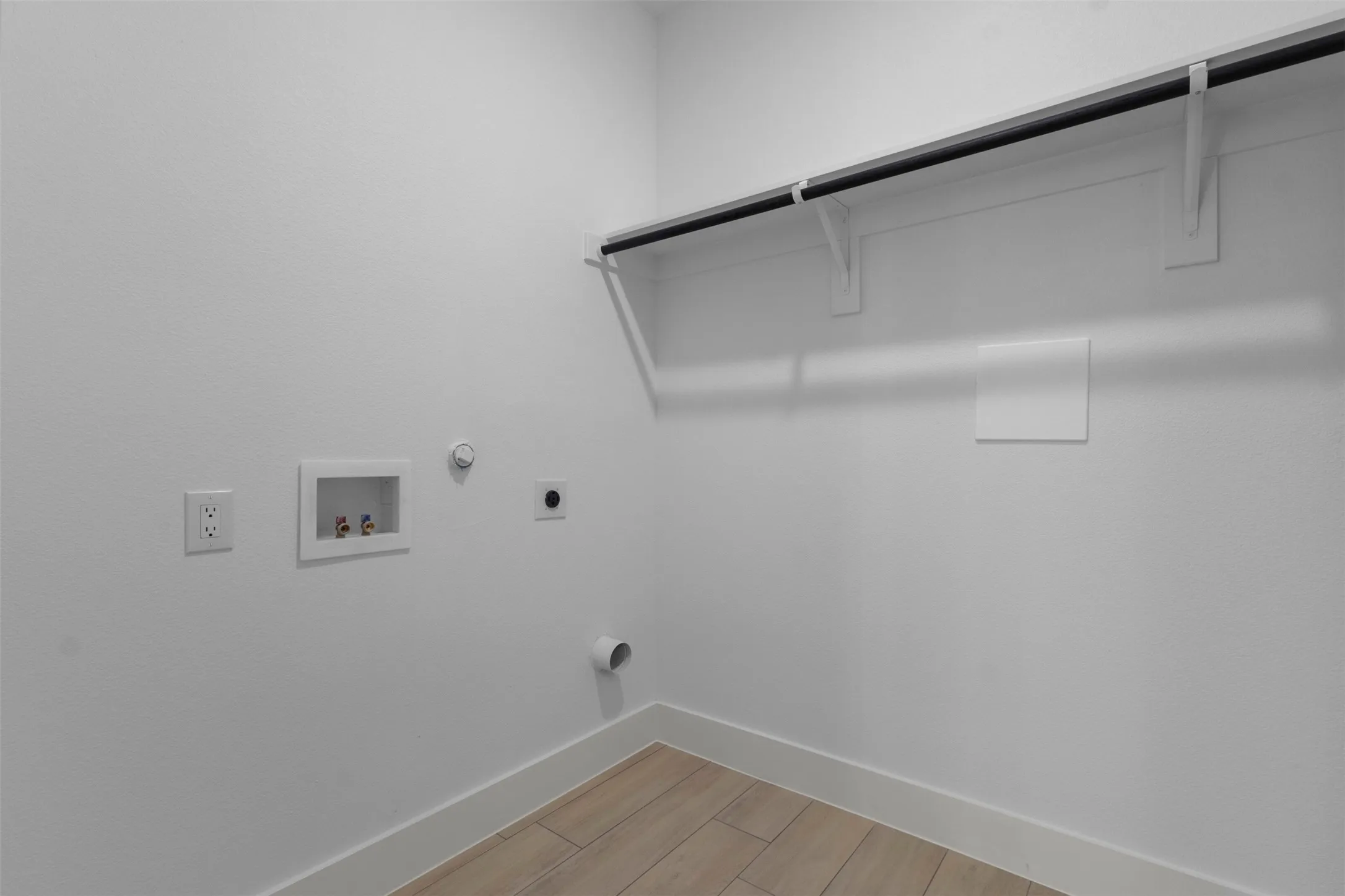 Laundry area featuring wood-finish flooring, a built-in hanging rod, and utility hookups