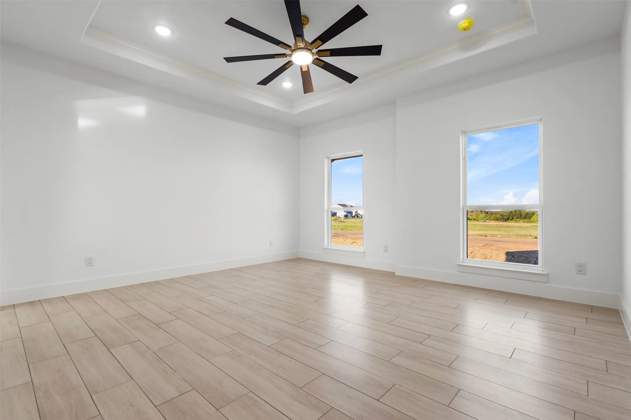 Tray ceiling with recessed lighting, ceiling fan with light fixture, wood-finish flooring, and two windows