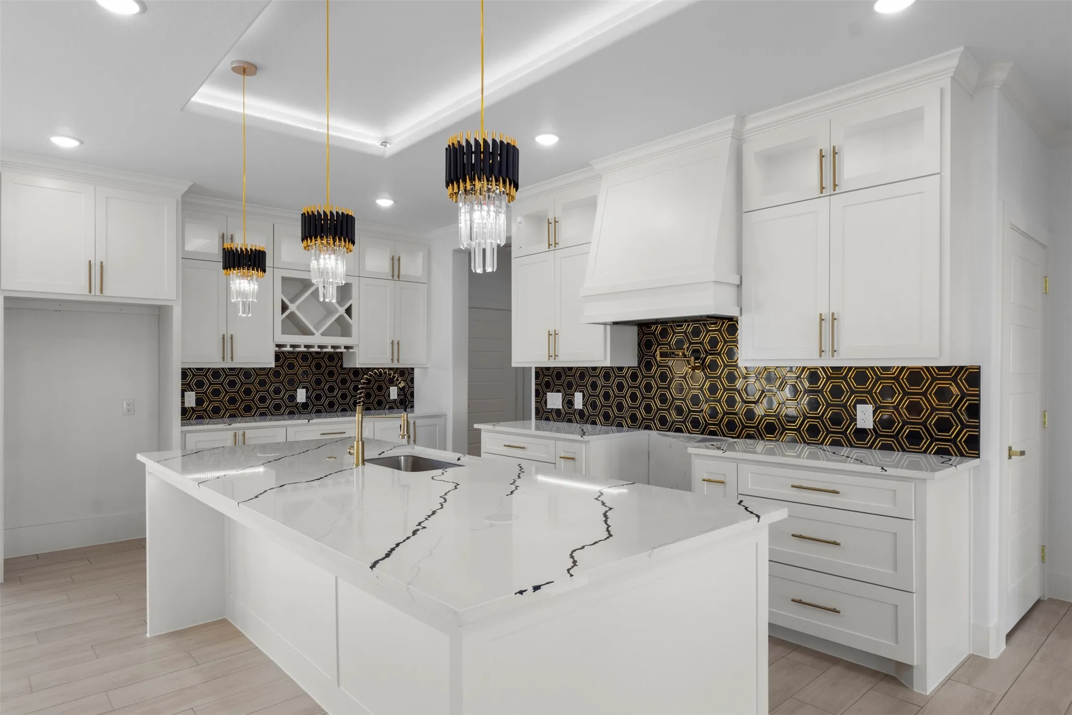 Kitchen featuring white cabinetry with gold-toned hardware, a spacious island with a veined countertop, a hexagon-patterned backsplash, and modern pendant lighting