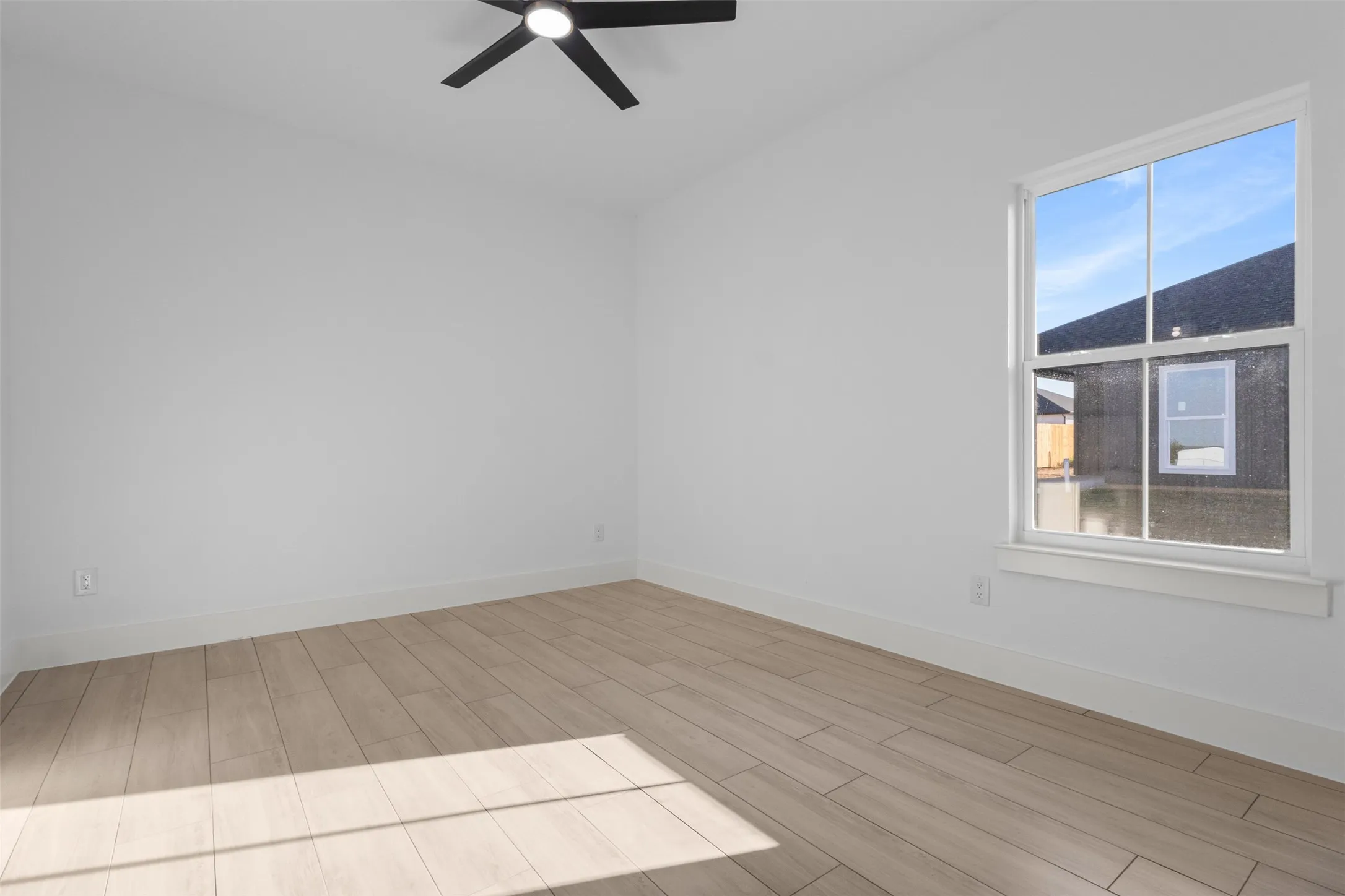 White walls, wood-finish flooring, white window trim, and a black ceiling fan with integrated lighting