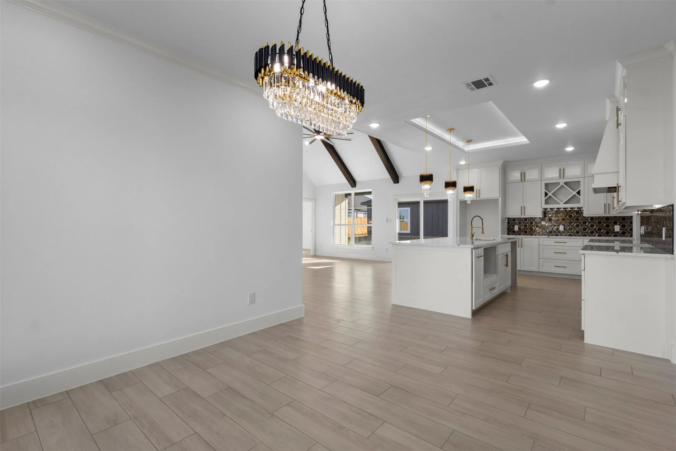 Wood-finish flooring, vaulted ceiling with exposed beams, pendant lighting, white cabinetry, and a kitchen island with integrated sink