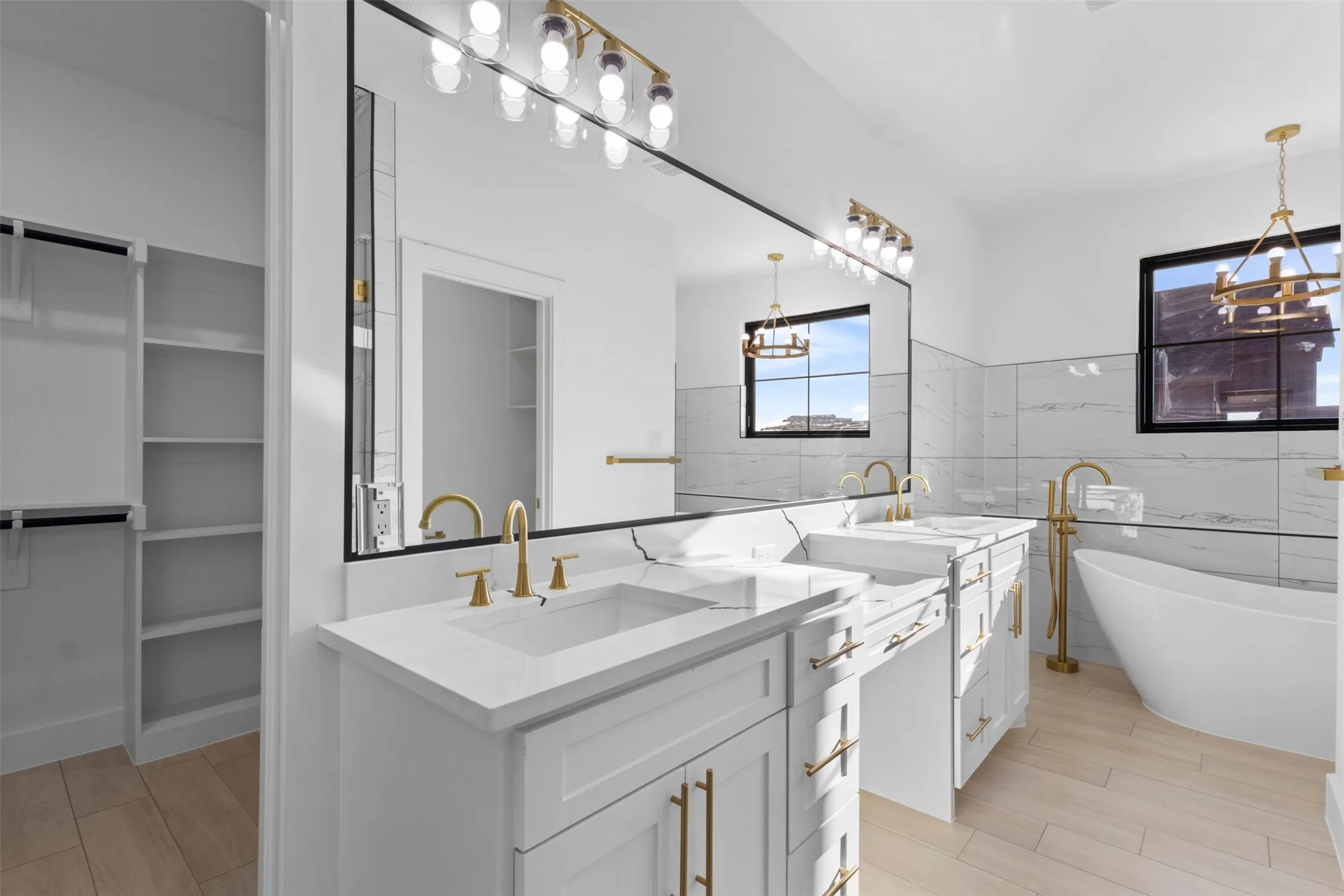 Dual vanities with white countertops, gold-finish fixtures, and a large mirror with integrated lighting