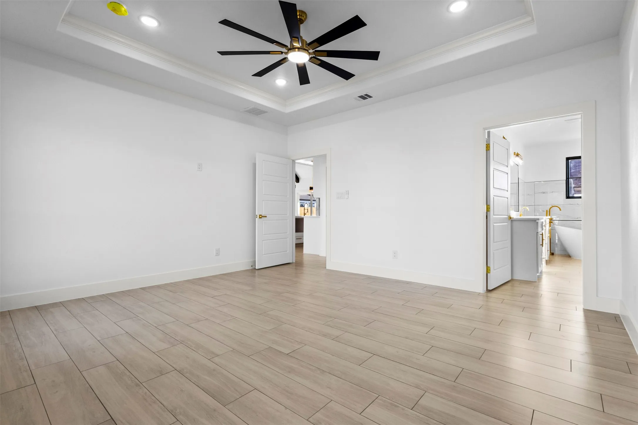 Tray ceiling with recessed lighting, ceiling fan with black blades, white paneled doors, and wood-finish tile flooring
