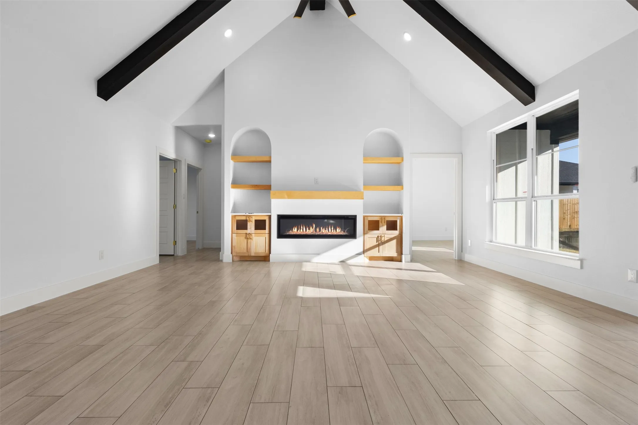 Vaulted ceilings with exposed dark beams, wood-finish flooring, built-in fireplace, recessed lighting, and large window